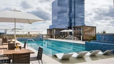 Luxury rooftop pool area with lounge chairs, umbrellas, and city view skyscrapers in the background.