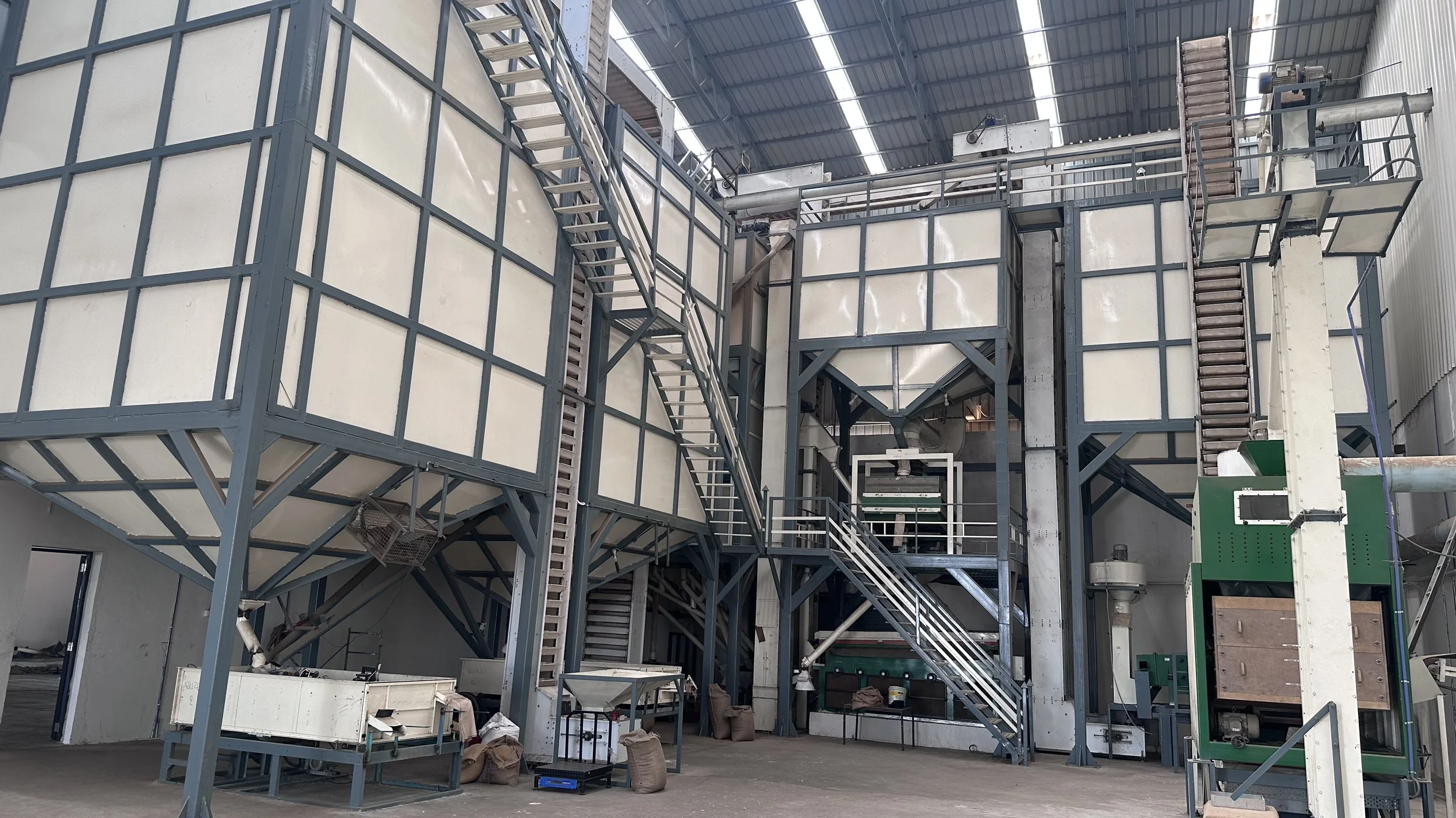 Industrial processing plant with large white and gray machinery, stairs, and walkways inside a warehouse.