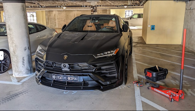 Black Lamborghini Huracan parked in a parking garage, surrounded by tools and equipment, including a floor jack, a toolbox, and a wrench.