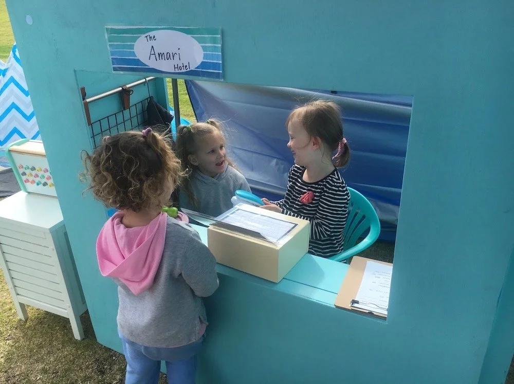 Three young girls talking and laughing at a window that says The Amari Hotel