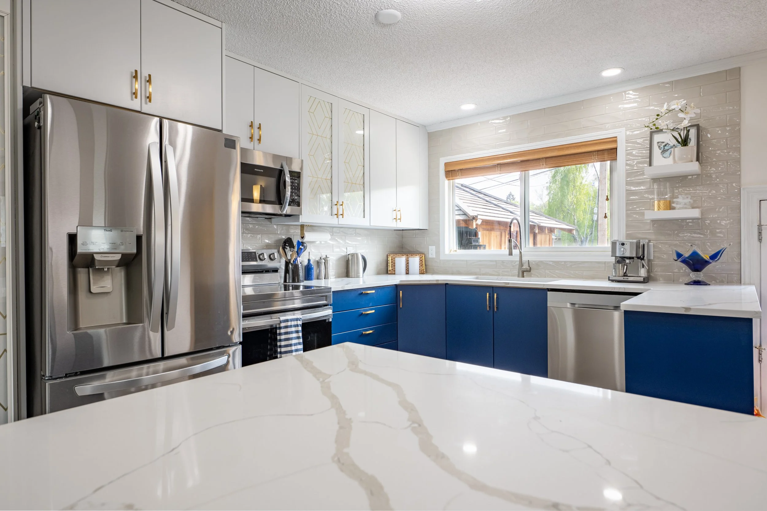 a beautiful white and blue kitchen is shown.  a grey veined quartz countertop is the feature of the room