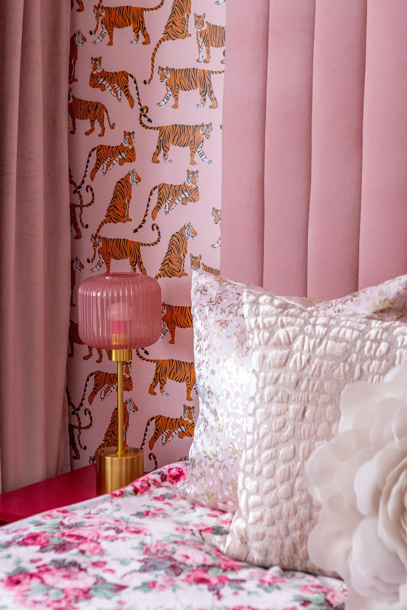 details of a pink bedroom is shown, including pink custom silk pillows, pink tiger wallpaper, pink drapes, and a pink custom tufted channel headboard