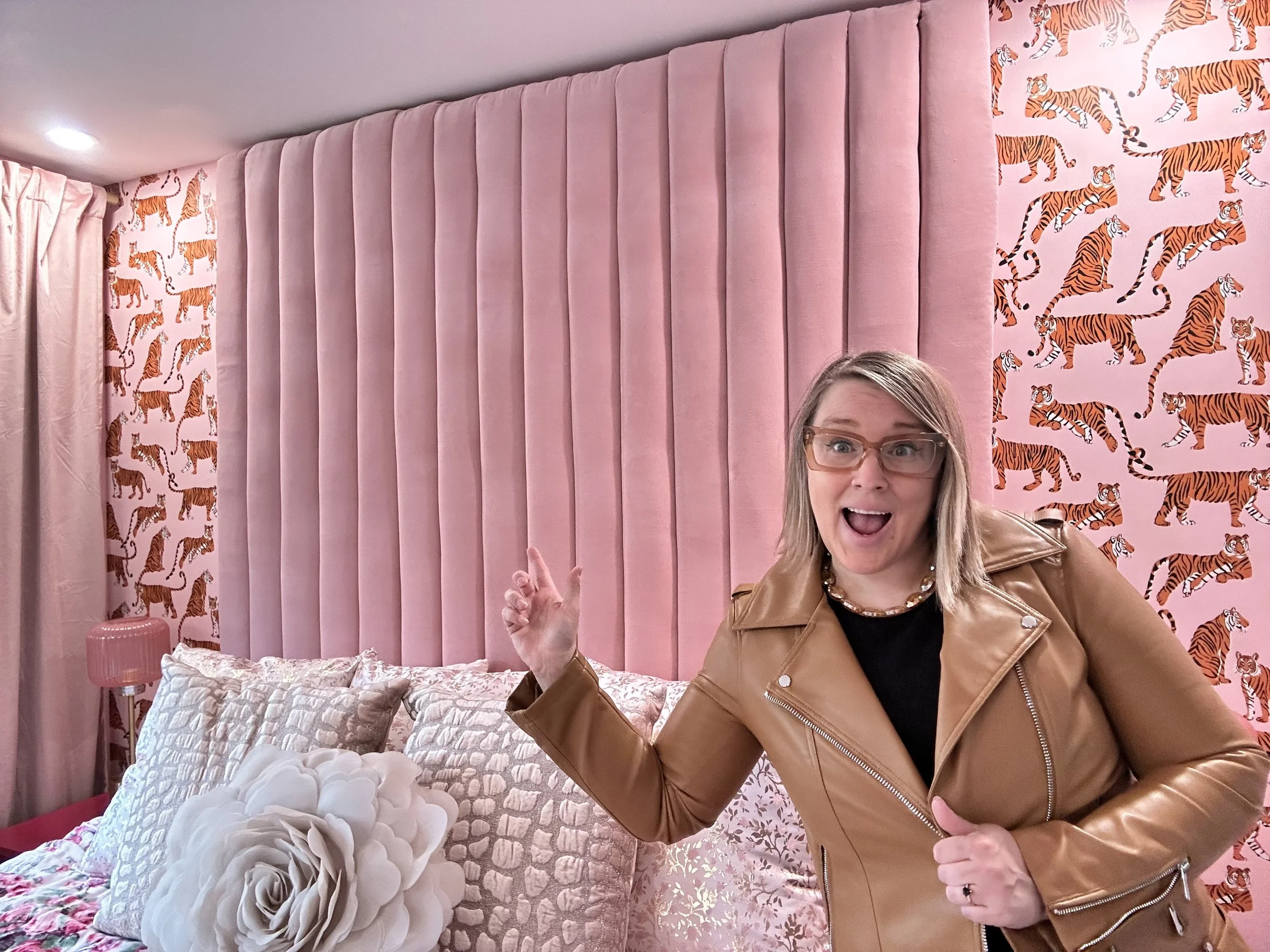 a pink bedroom for adults is shown. a designer is pointing to the custom channel tufted headboard she made from scratch