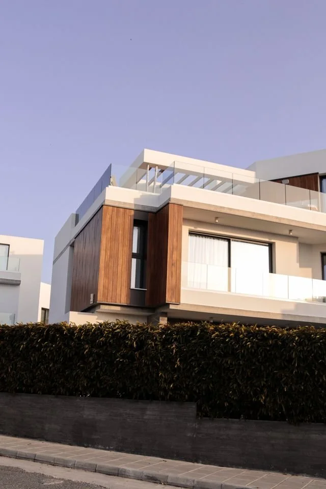 Modern house with white exterior, wood panel accents, roof terrace and blue sky.