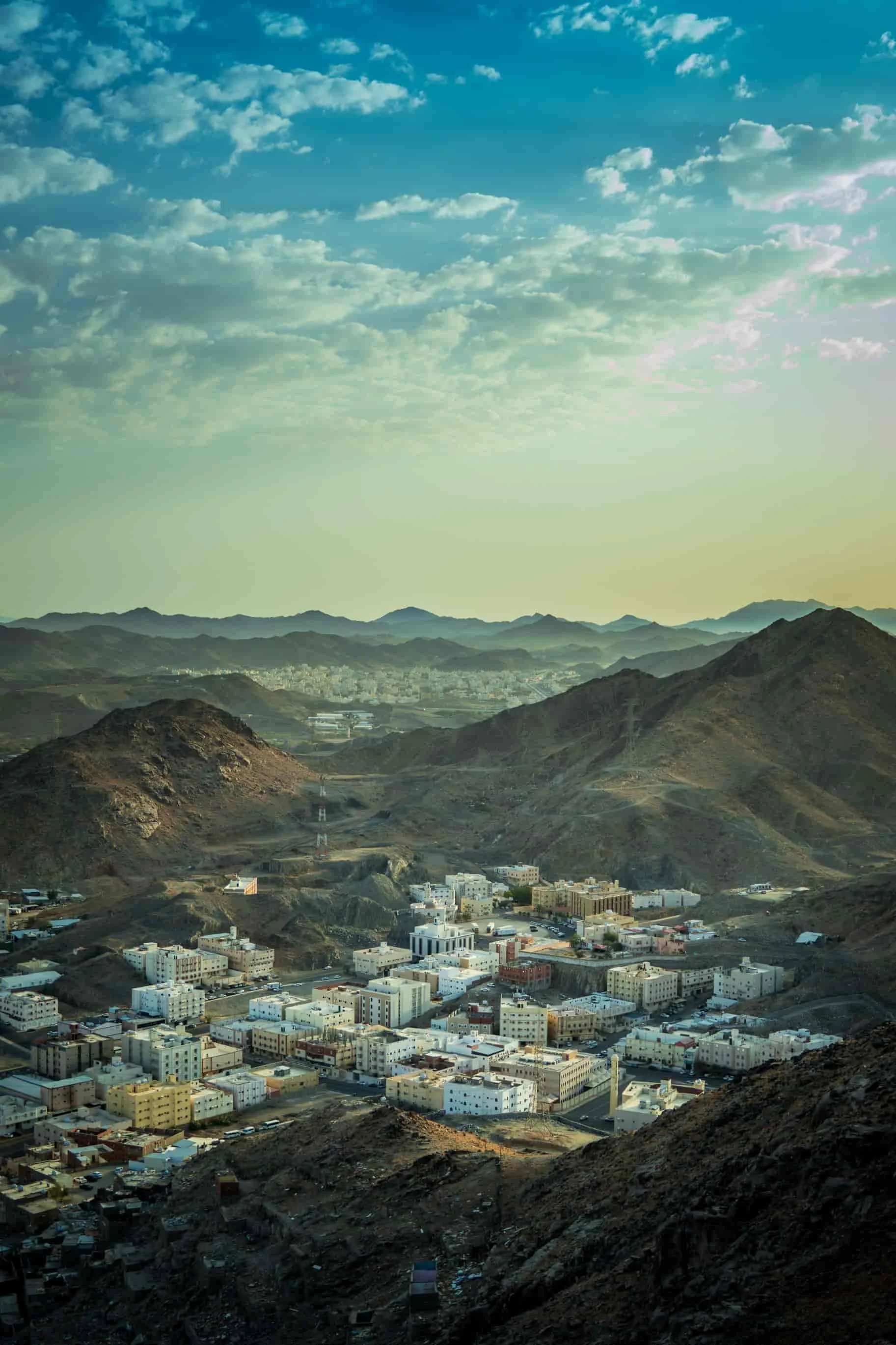 A view of a city at the base of a mountain range with scattered buildings in Saudi Arabia.