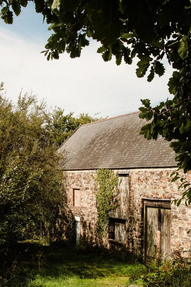 A rundown stone and tile barn surrounded by trees, ready for conversion.