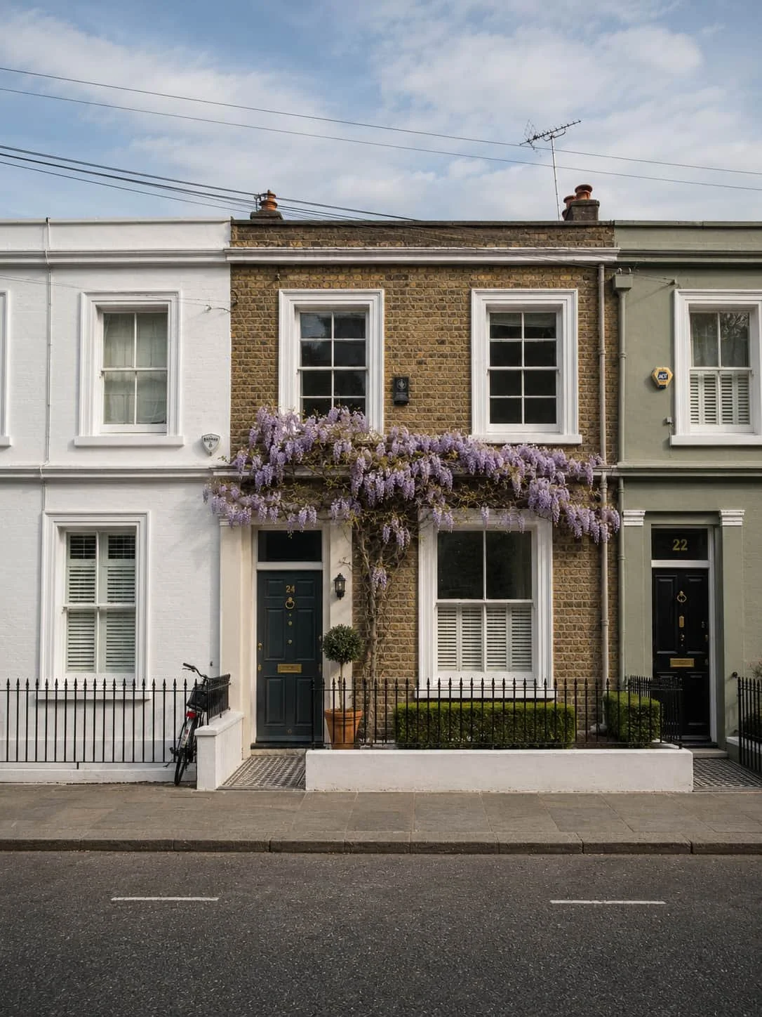 A brick mid-terraced house with white windows and wisteria.