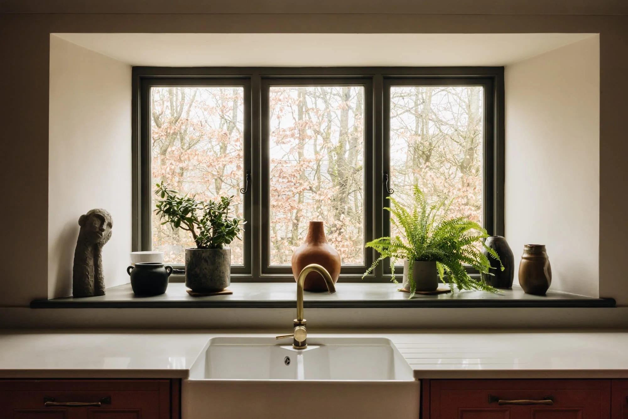Kitchen sink view through a window with potted plants and decorative items on the windowsill