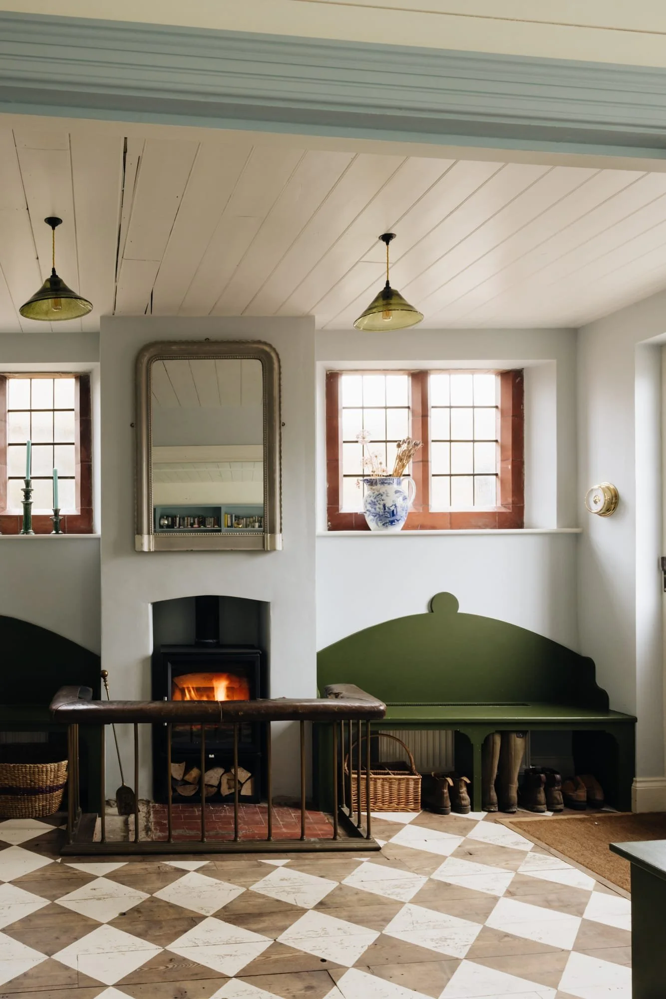 Cozy living room with a fireplace, green bench, checkered wooden floor, and windows with red brick frames.
