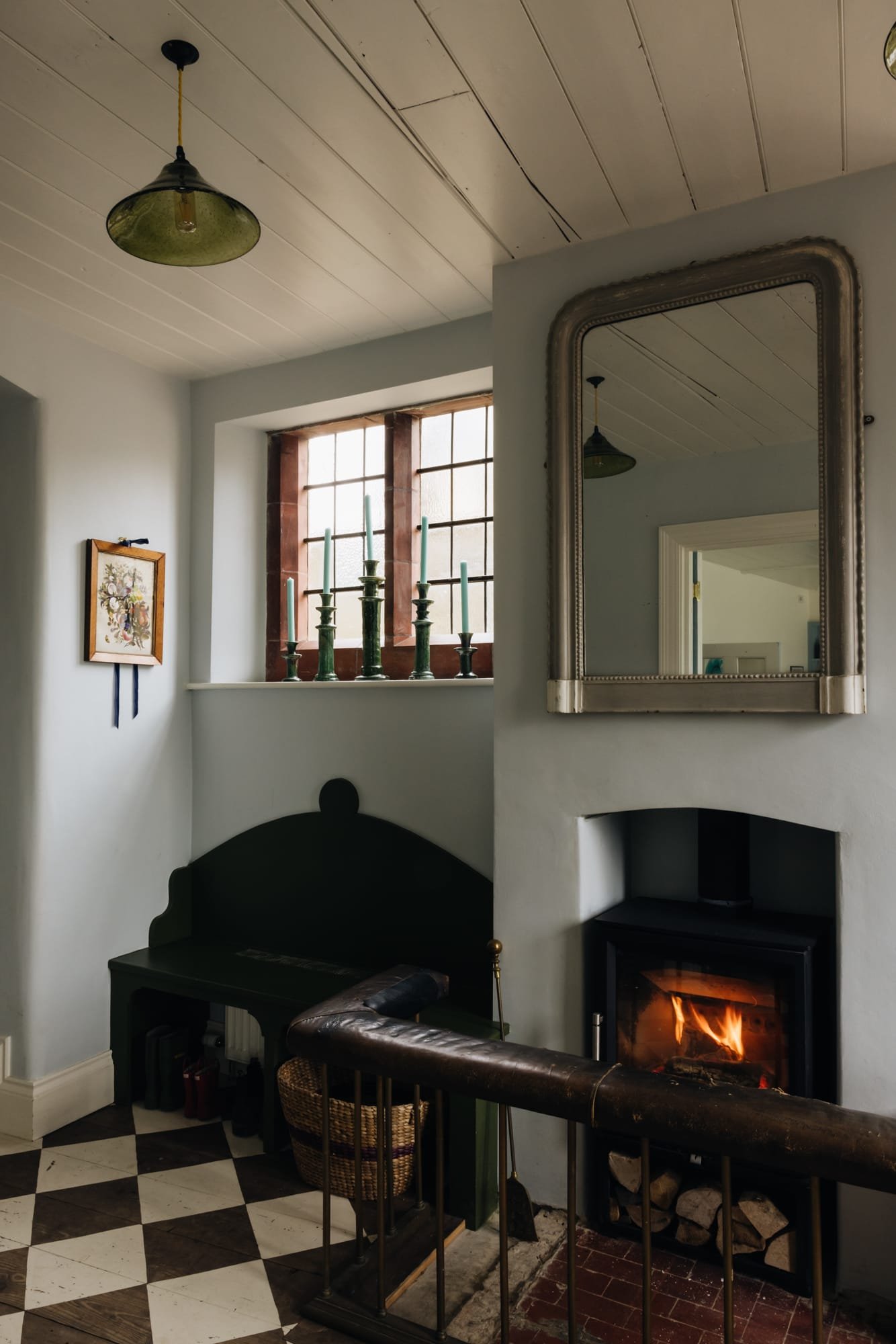 A cozy living room corner with a fireplace, a large mirror, a window with candles, and vintage decor.
