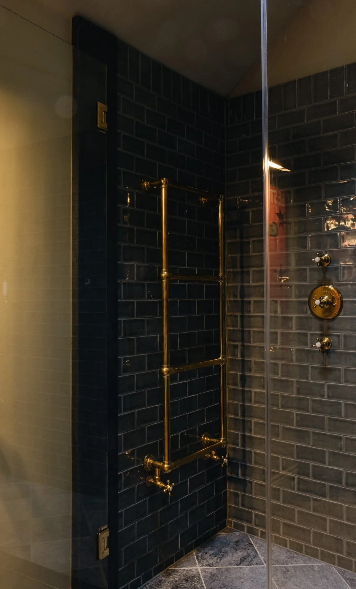 Black tiled shower with vintage brass fixtures and piping.
