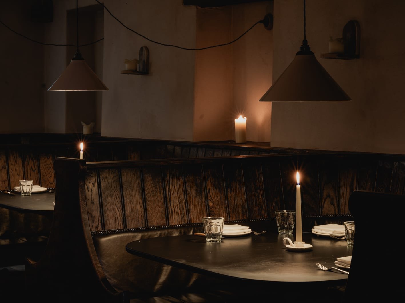 A dimly lit restaurant with candlelit tables, dark wooden furniture, and candles creating a cozy atmosphere.