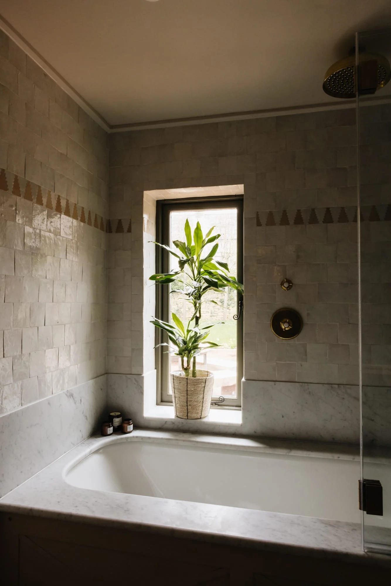Bathroom with a bathtub beneath a window, which has a potted plant on the sill, and small candles on the corner of the tub.