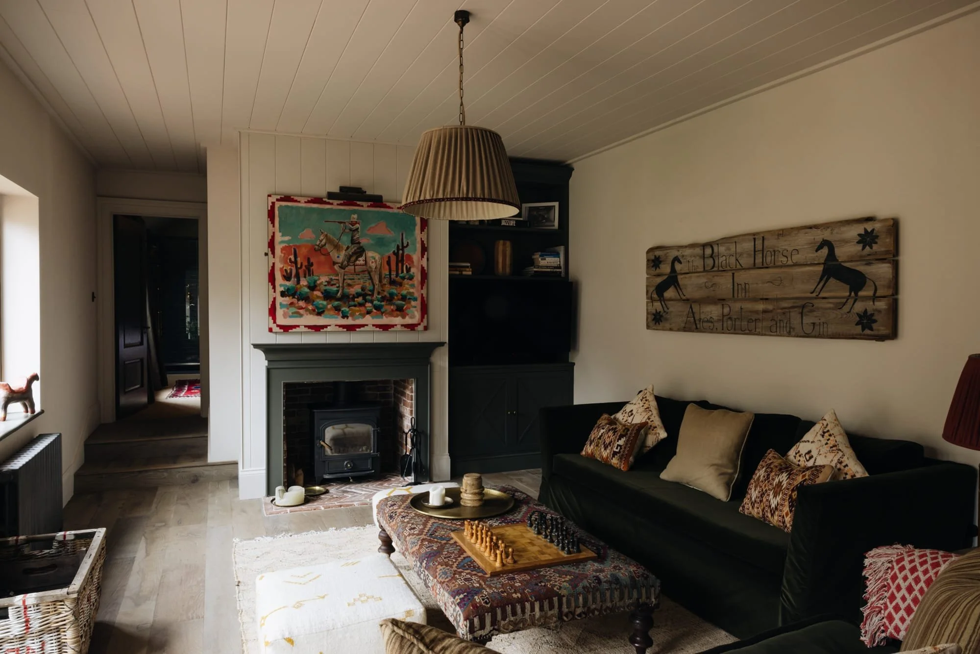 Living room with a fireplace, colorful wall art, black sofa with patterned pillows, wooden coffee table with a chess set, and wall decorations including a wooden sign and a tapestry.
