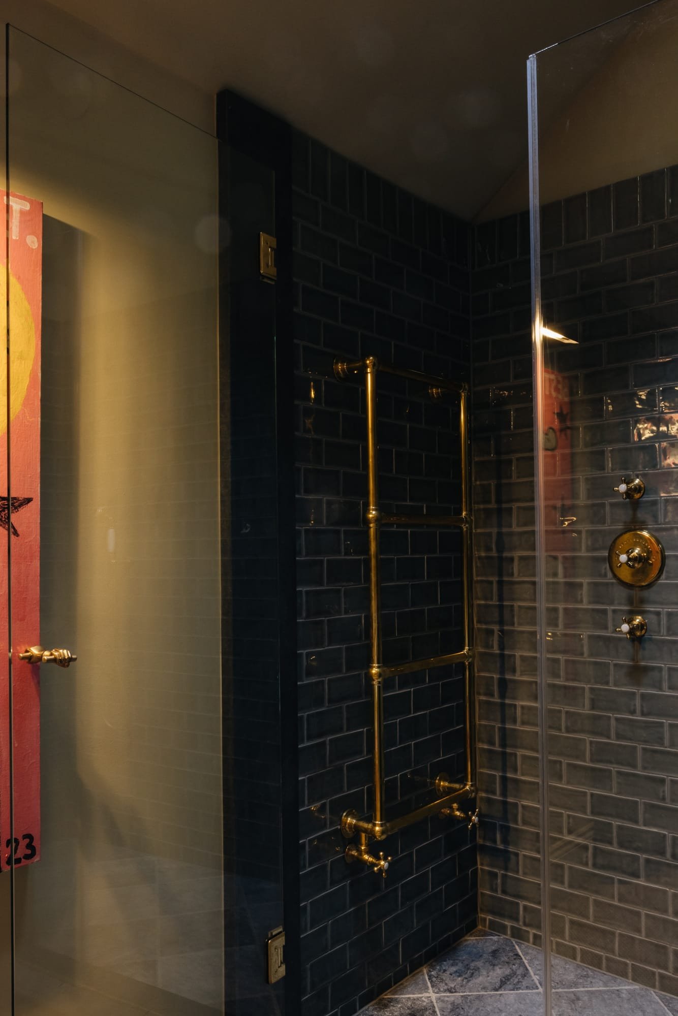 Bathroom shower with dark gray brick tiles, gold pipe fixtures, and a partial glass shower door.