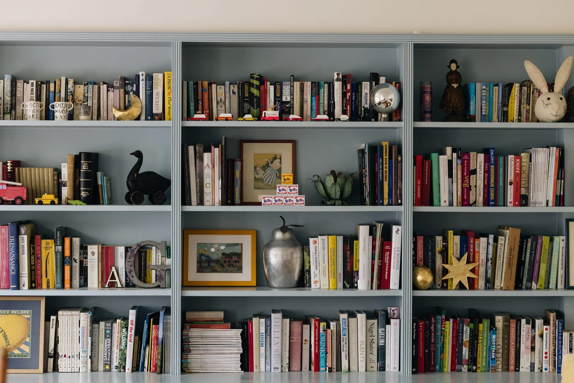 Bookshelf filled with colorful books and decorative objects including figurines, framed pictures, and small sculptures.