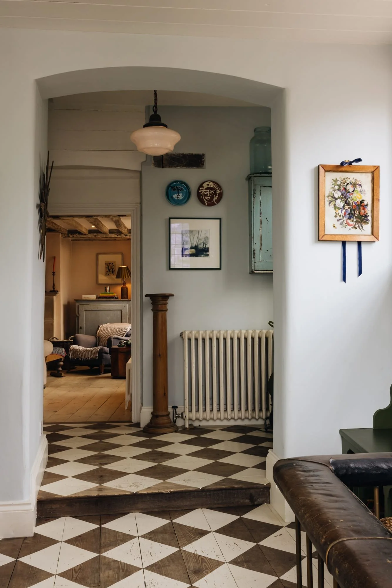 View of a hallway leading to a cozy living room with vintage and rustic decor, checkered tile floor, decorative plates on wall, and soft lighting.