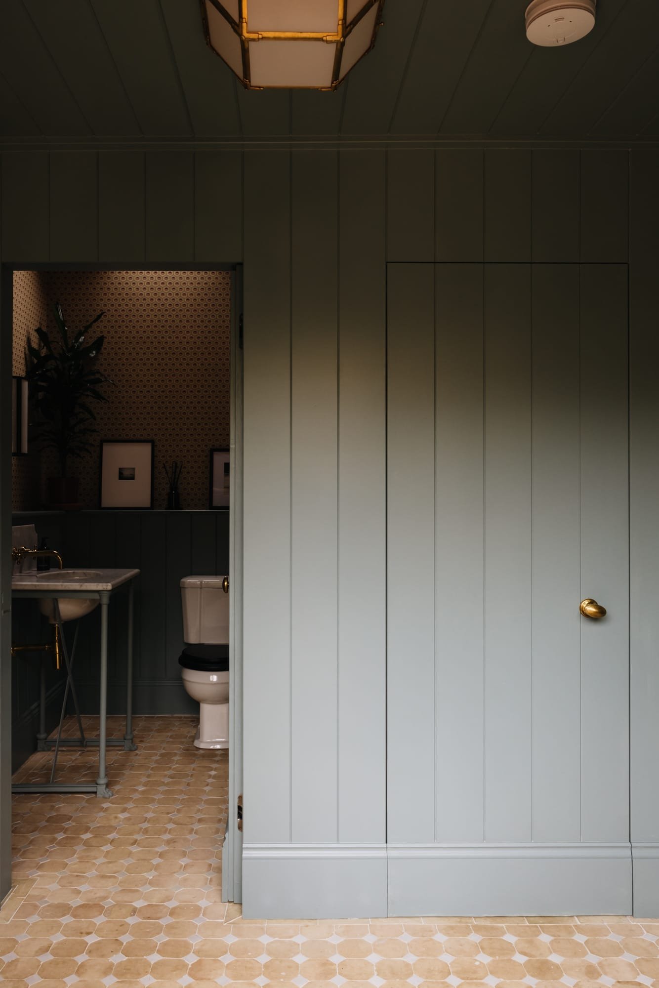 View into a bathroom through a partially open door, showing a toilet, a small sink, and framed pictures on the wall.