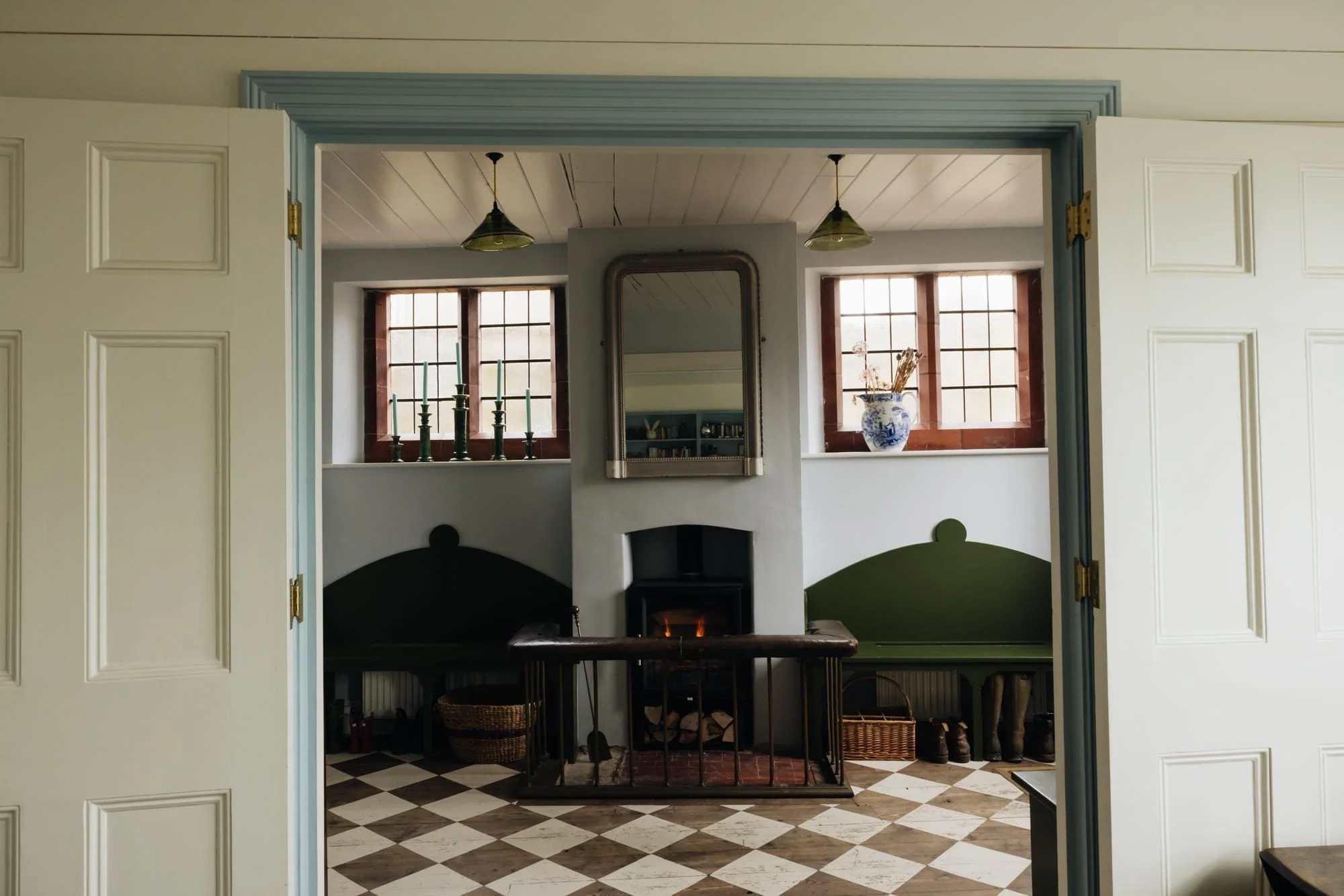 Interior view of a cozy room with two windows, a fireplace, mirror, and vintage decor, seen through an open door.