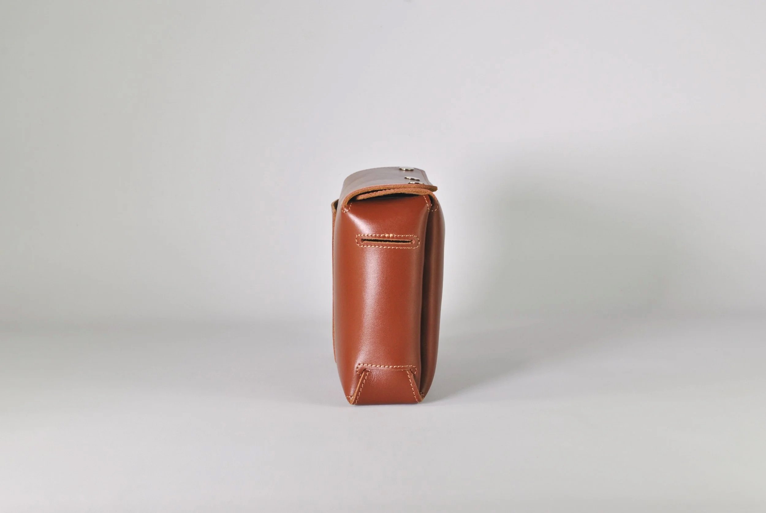 Side view of a brown leather bag on a plain white background.