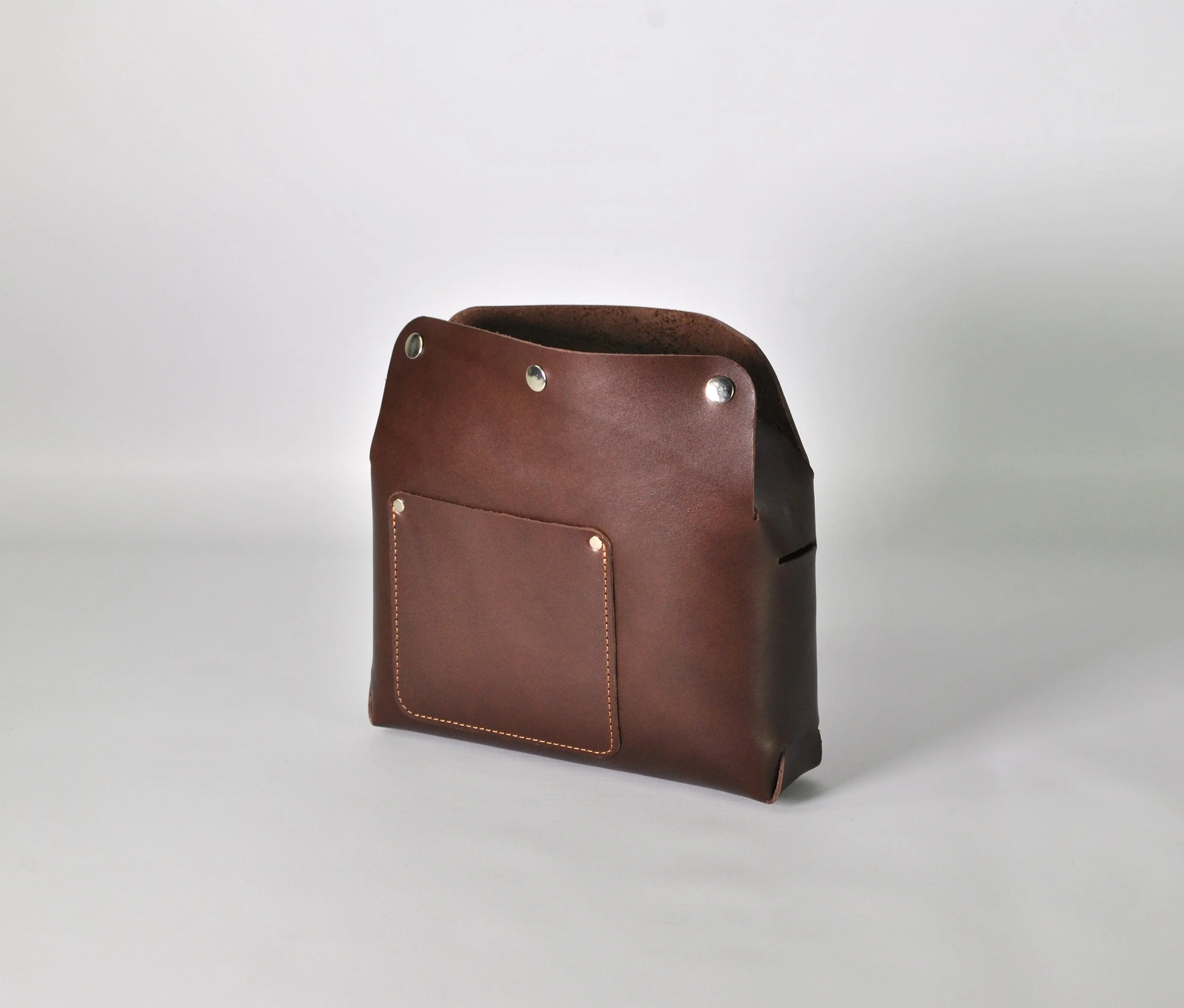 Brown leather bag with a front pocket, sitting on a plain white surface.