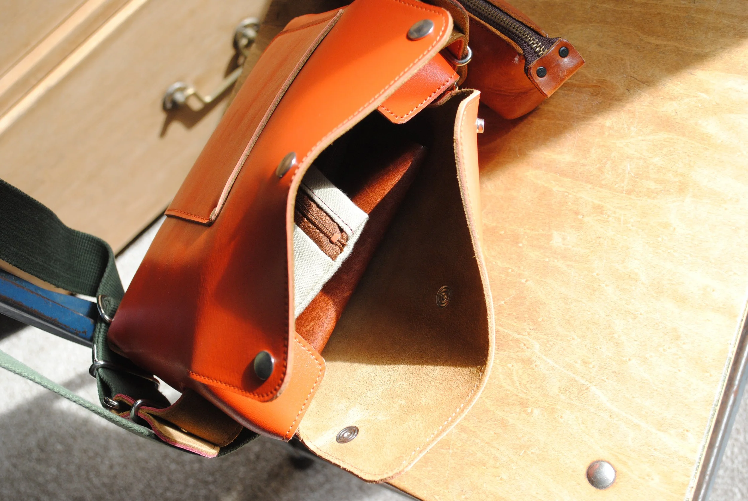 An open brown leather bag with a small beige and brown pouch inside, placed on a wooden surface.
