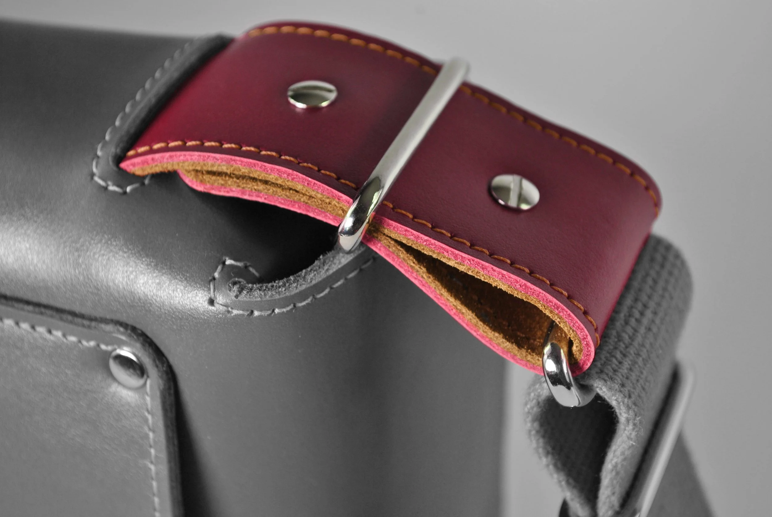 Close-up of a gray leather bag with a red connector.