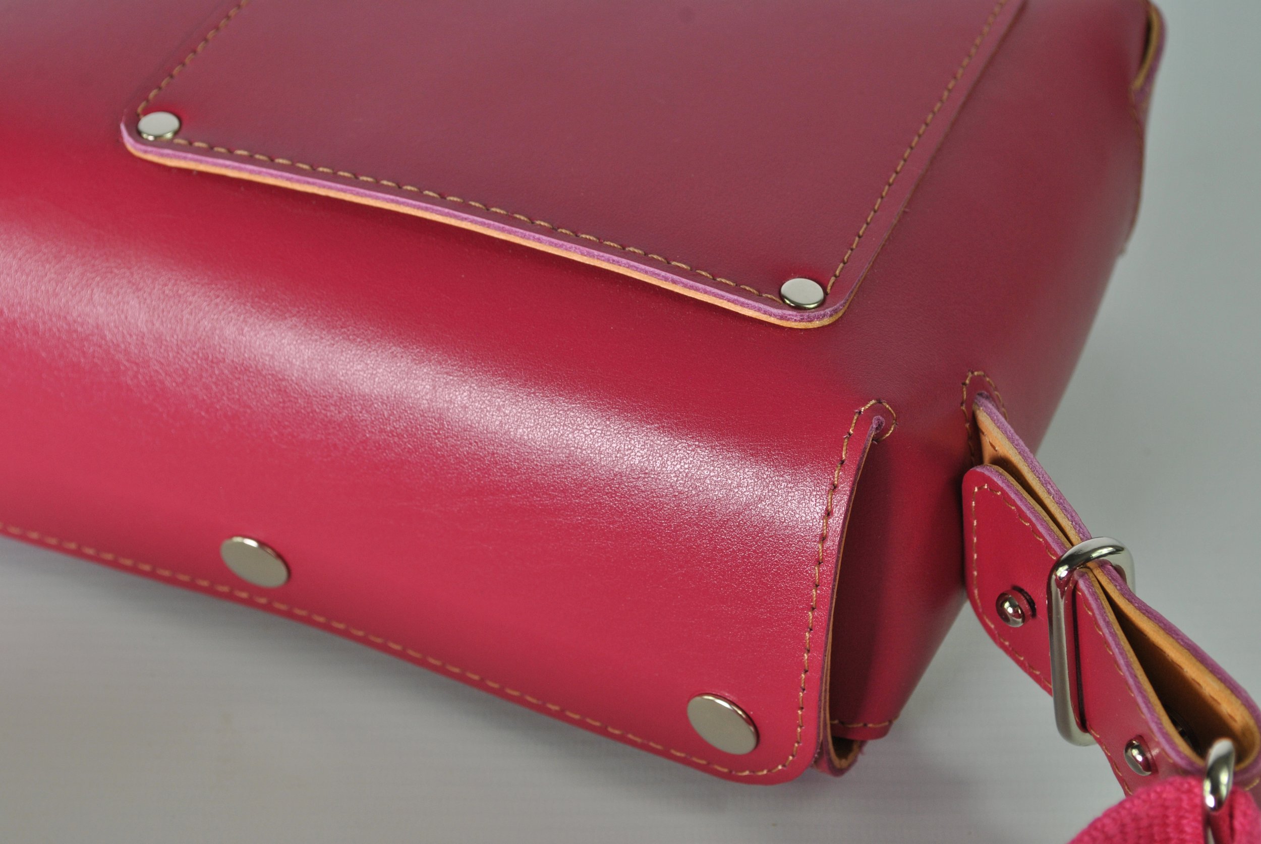 Close-up of a pink and purple leather handbag with silver hardware, showing the bottom corner, stitching, and part of the strap.