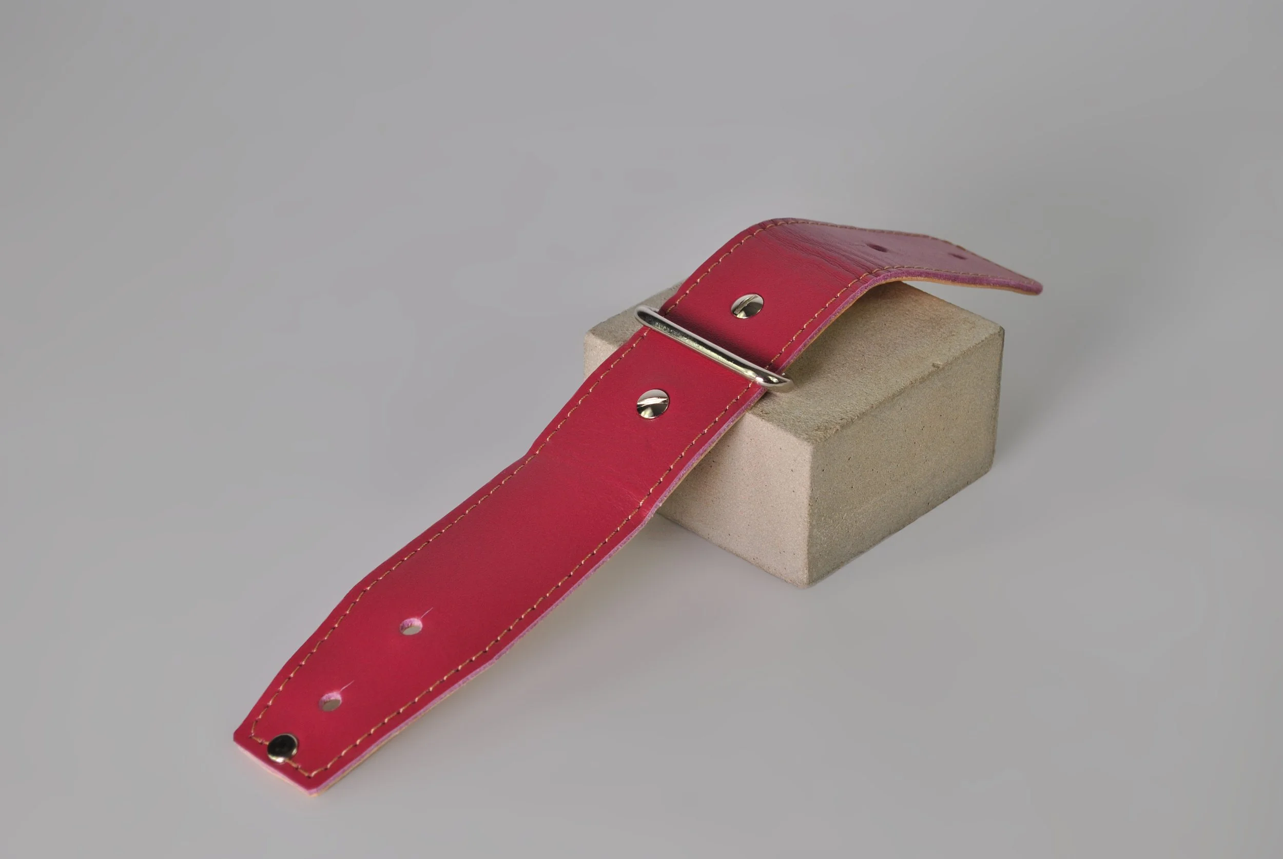 A pink leather connector with a silver hardware resting on a concrete block against a plain background.