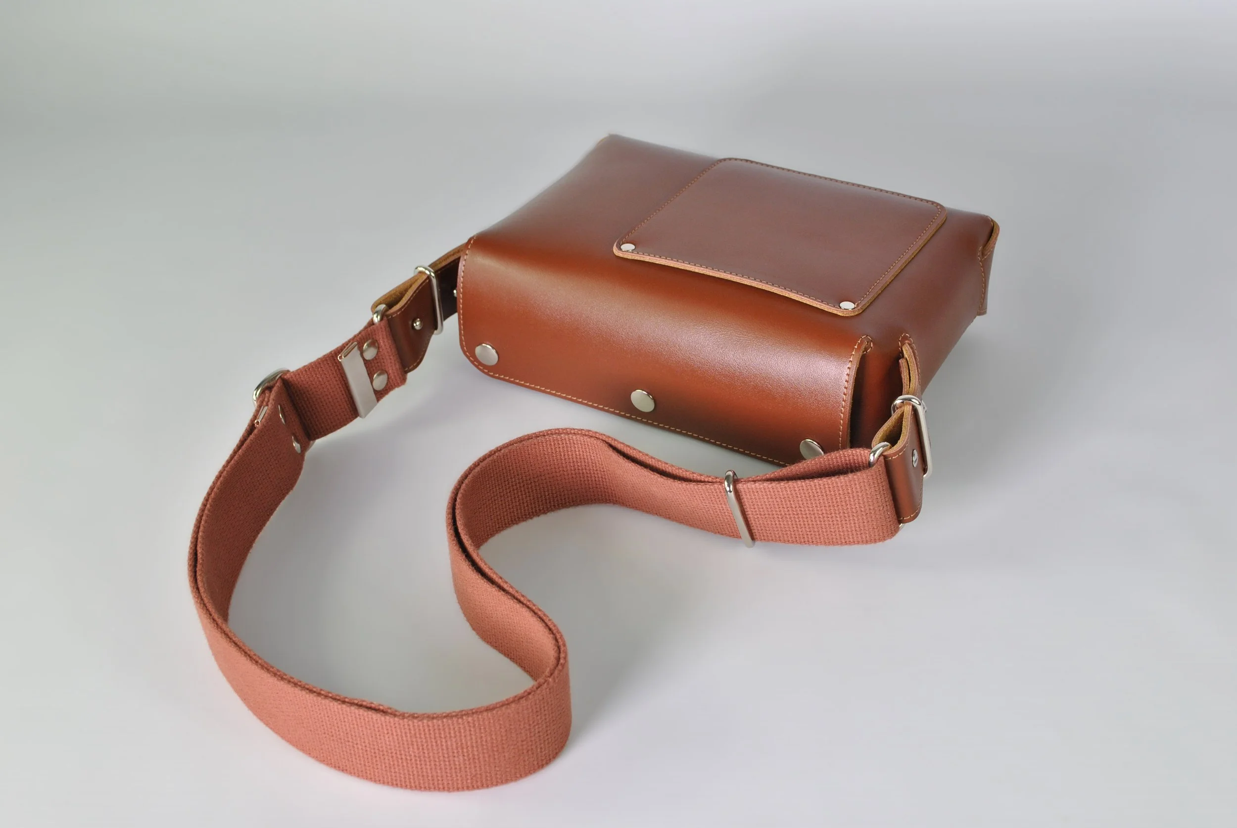 Brown leather handbag with an adjustable pink fabric strap on a white surface.