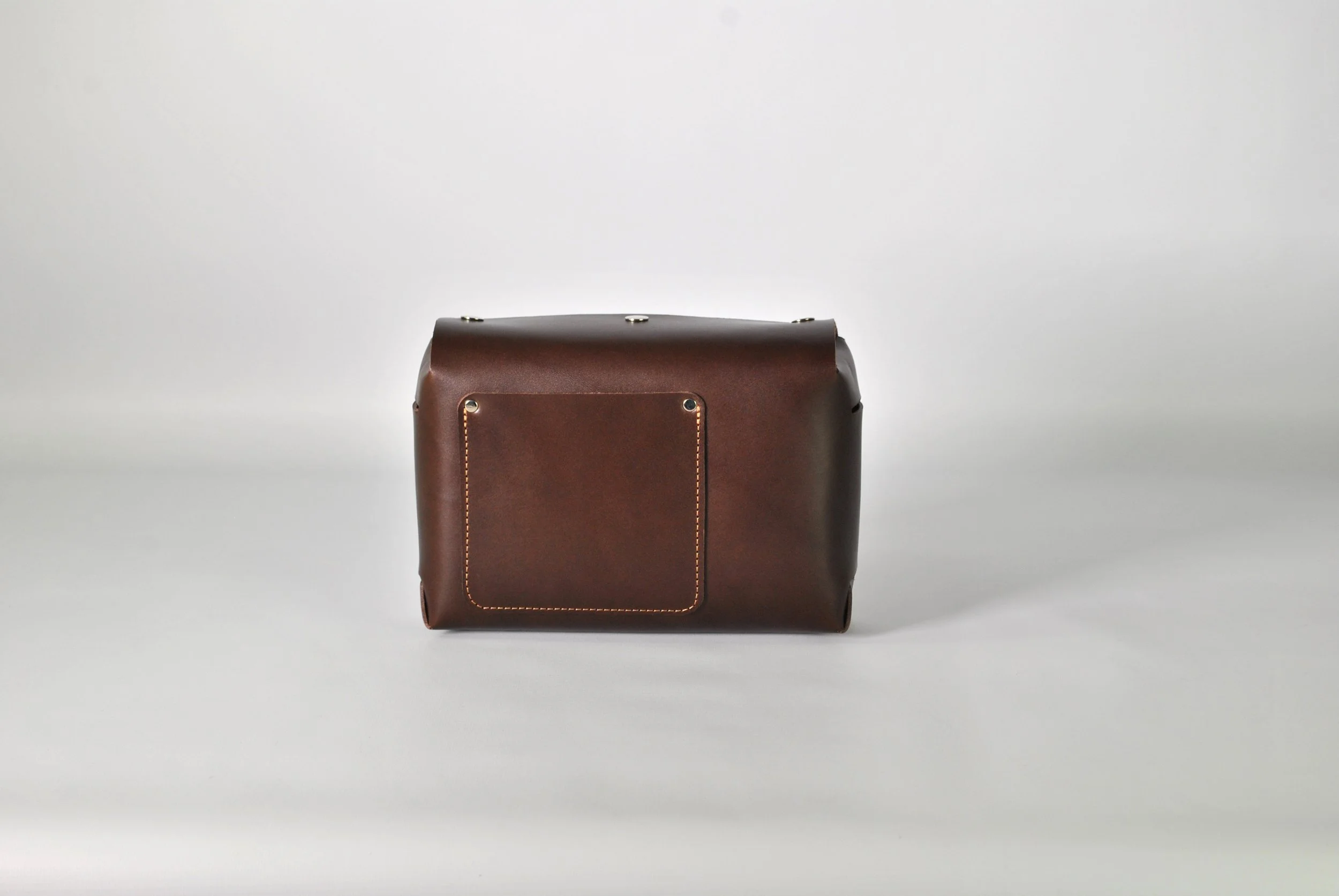 Brown leather bag with a front pocket and metal hardware on a plain white background.