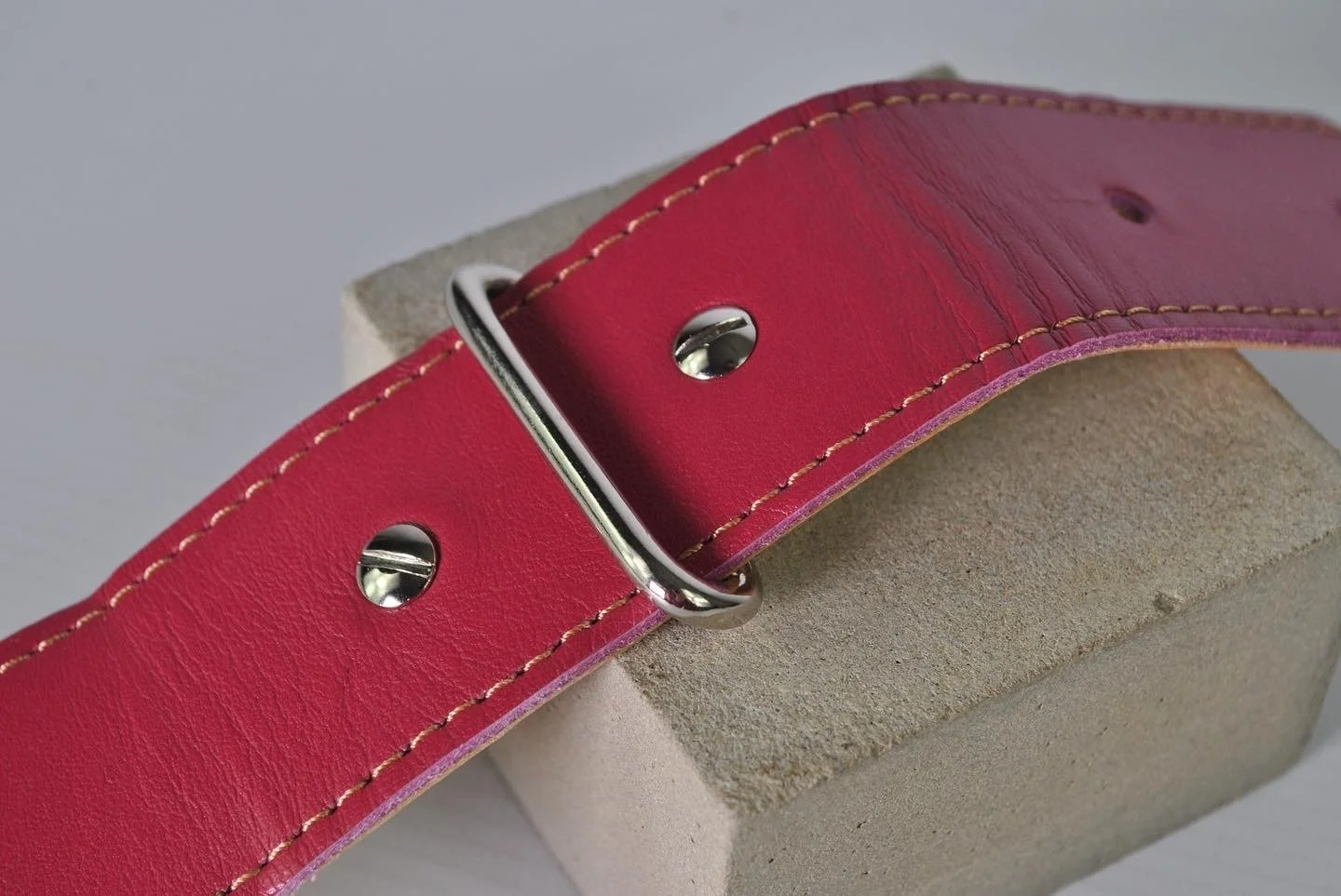 A close-up of a pink connector with silver hardware placed on a grey surface.