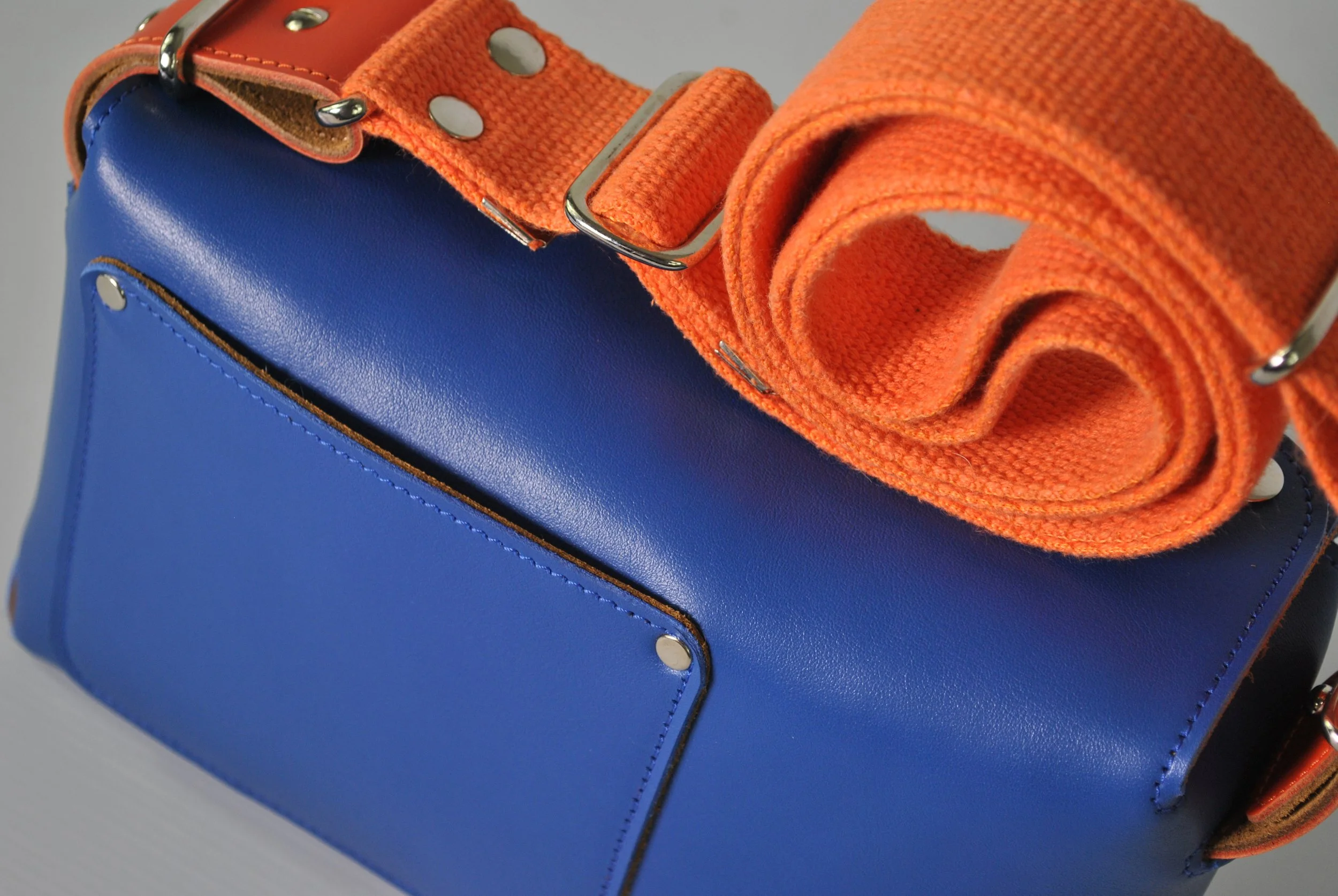 A blue leather handbag with an orange fabric strap wrapped around its handle.