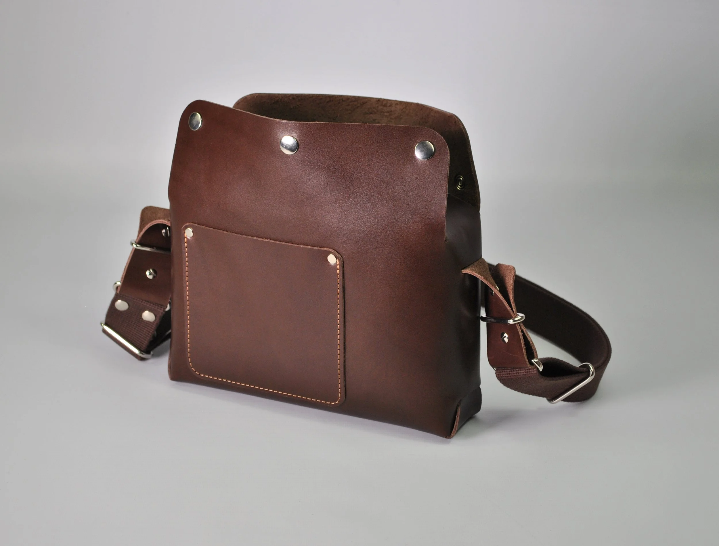 Brown leather messenger bag with adjustable strap and silver hardware on a light gray background.