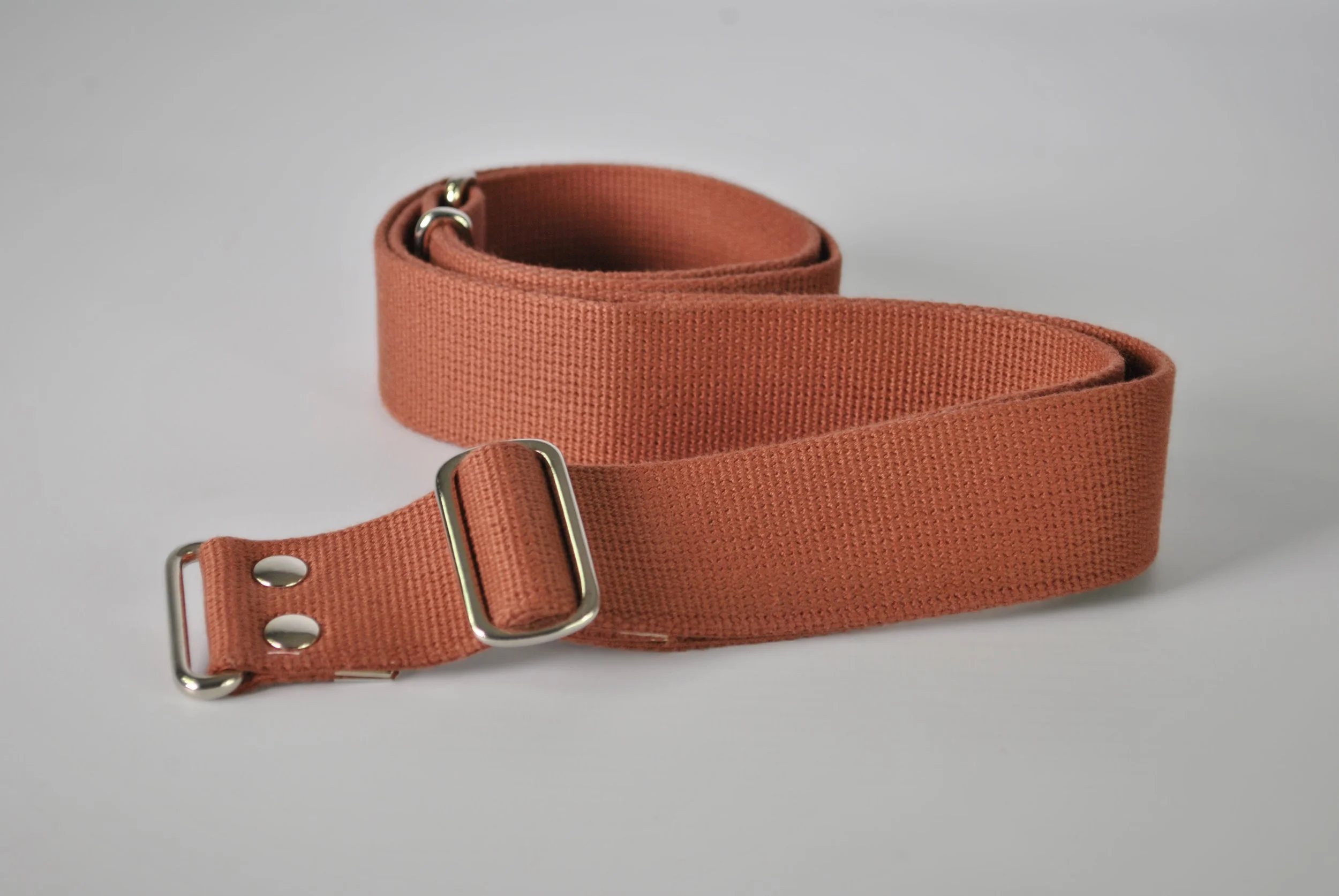 A rolled-up cotton strap with silver metal hardware for the And Roam carry system.