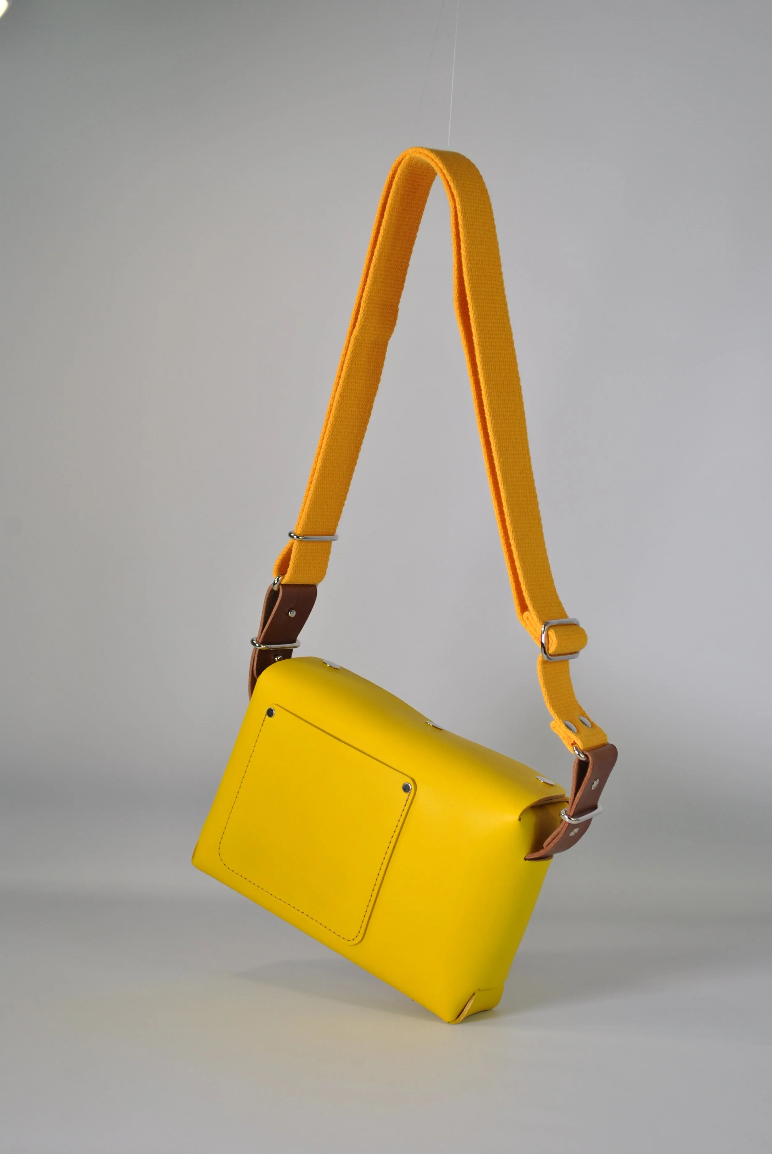 Yellow handbag with brown accents and a yellow strap hanging against a plain gray background.