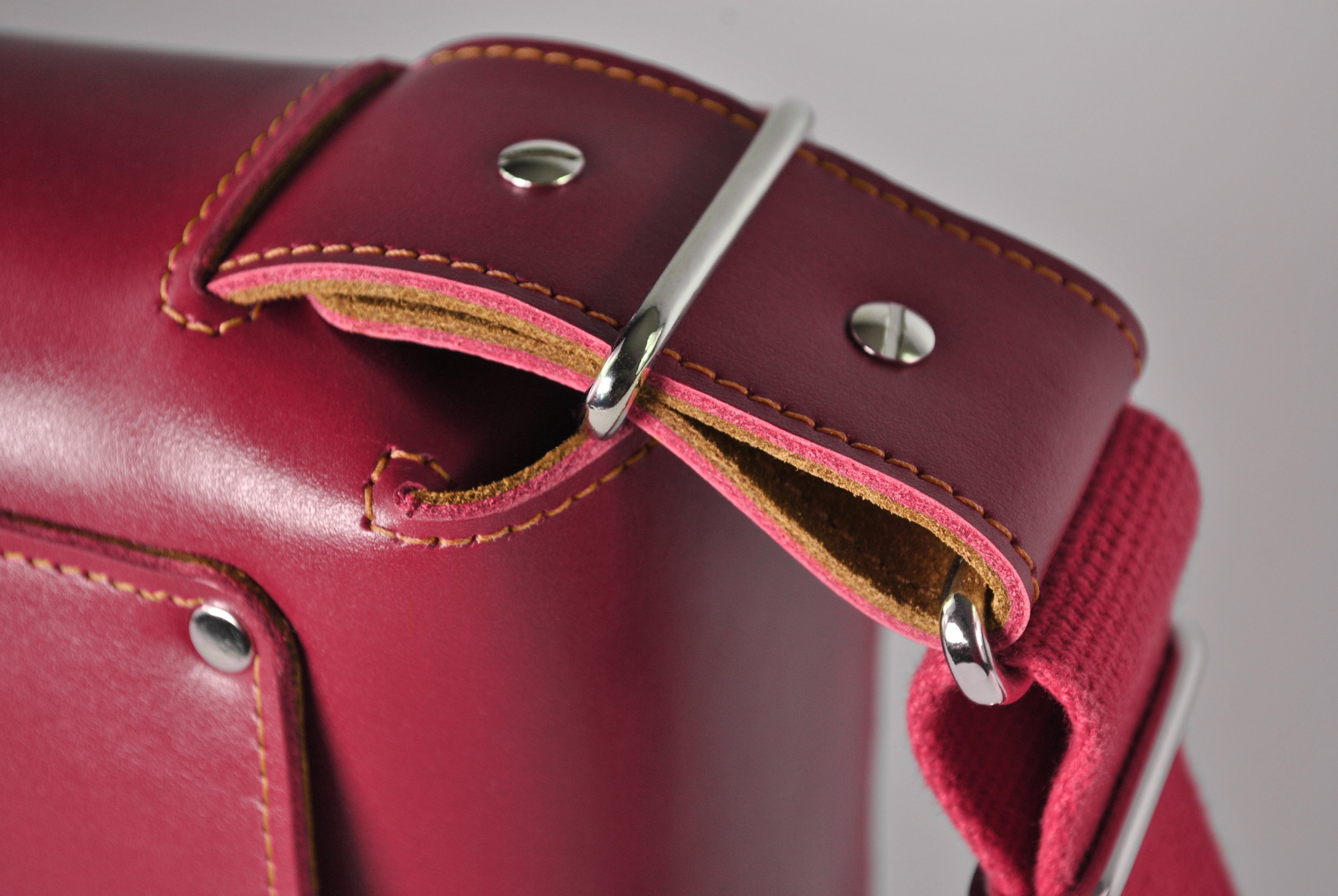 Close-up of a red leather bag with yellow stitching, metal rings, and a pink fabric strap.