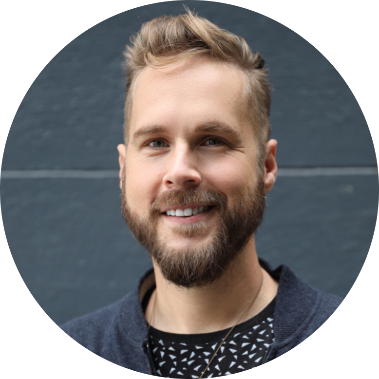 Headshot of John Marble smiling, with short light hair and a beard, wearing a dark jacket against a gray background.