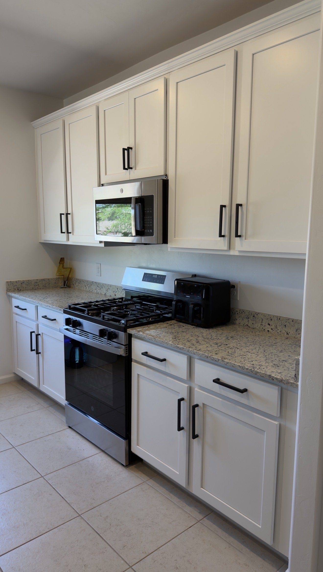 Kitchen with white cabinets, black handles, granite countertops, black stove, microwave, and small black appliance on countertop.