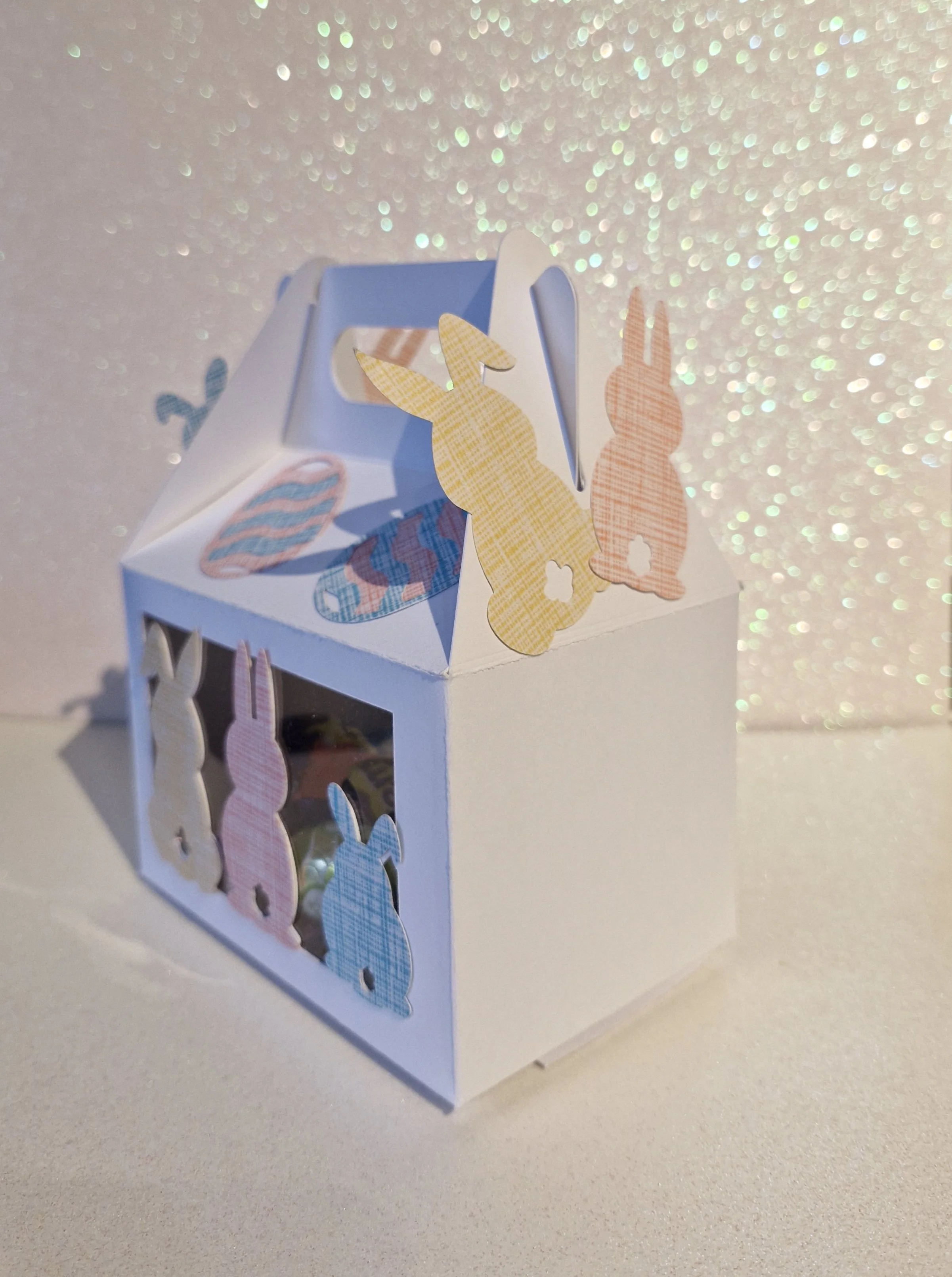  Includes a selection of mini chocolate eggs. Cushioned with pastel coloured tissue paper to prevent shifting. Sturdy gable-style box with carry handle.