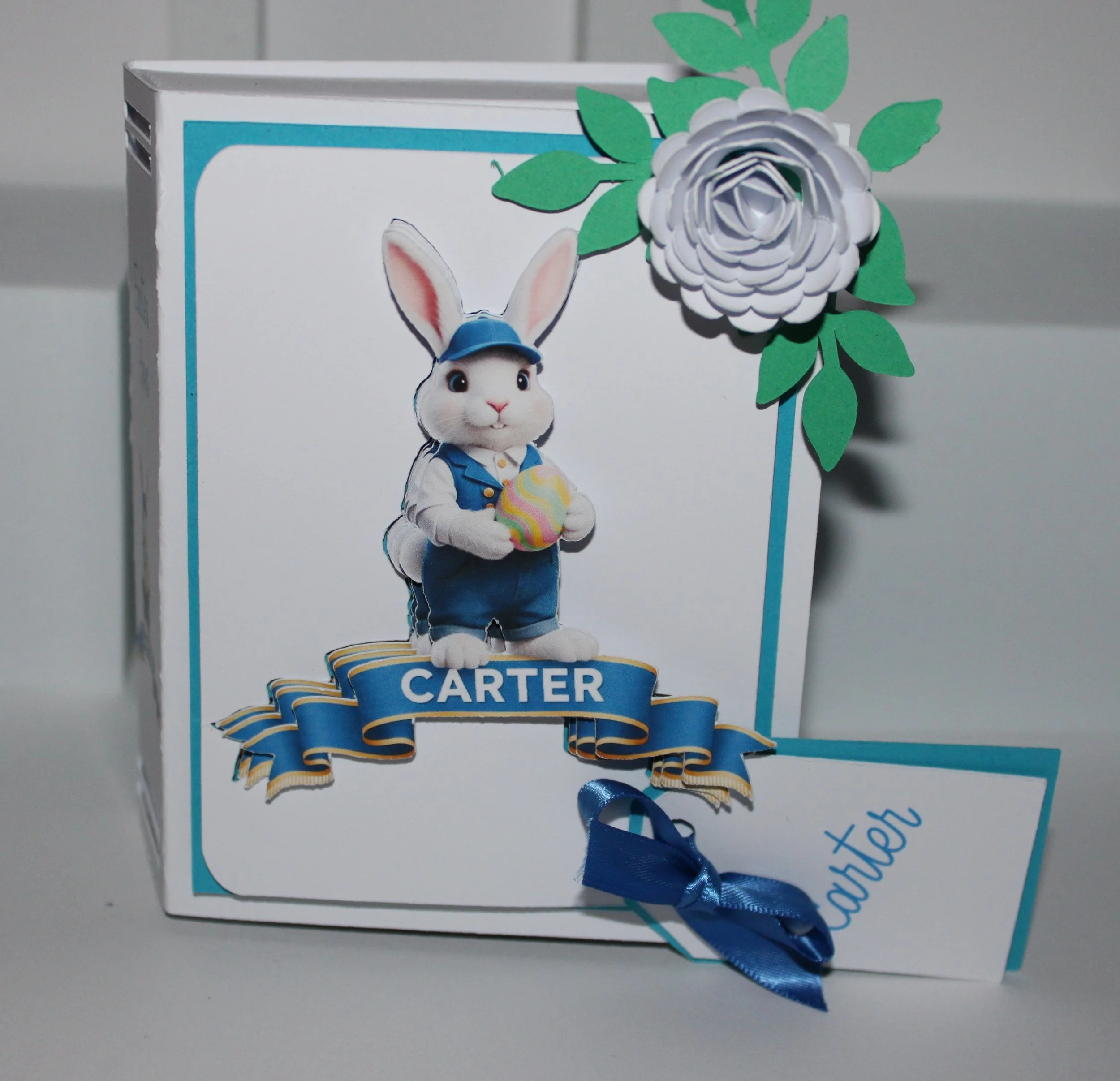 A personalised gift tag is attached for your message.

Open the box to reveal a tissue-paper-lined interior, thoughtfully arranged and filled with mini chocolate eggs. The spine is inscribed with "Happy Easter" alongside the recipient’s name, creatin