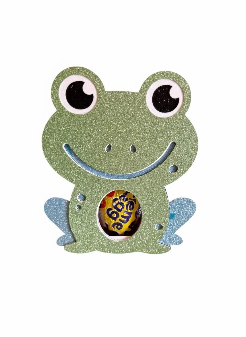 Easter Gift Box! 
Made with care and attention to detail. The box features a charming frog silhouette with subtle embossed details for the eyes and limbs. A small circular window at the front showcases a single decorated Easter egg held securely insi