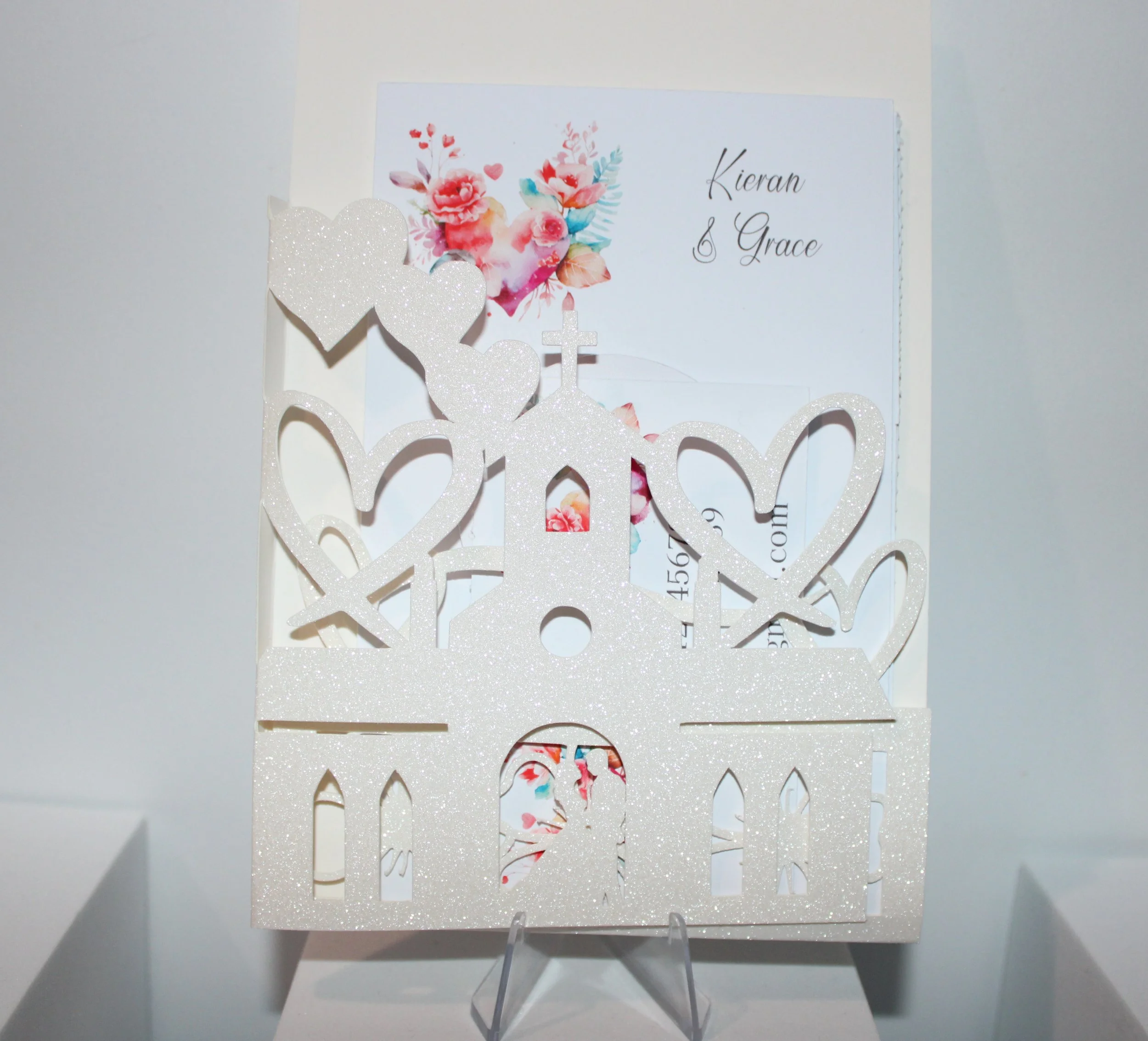 UNIQUE CHURCH INVITATION PACKAGE! Introducing our exquisite invitation card with a intricately cut church to the front of the invitation. Adorned with shimmering white glitter and delicately cut hearts flowing off the church. #004