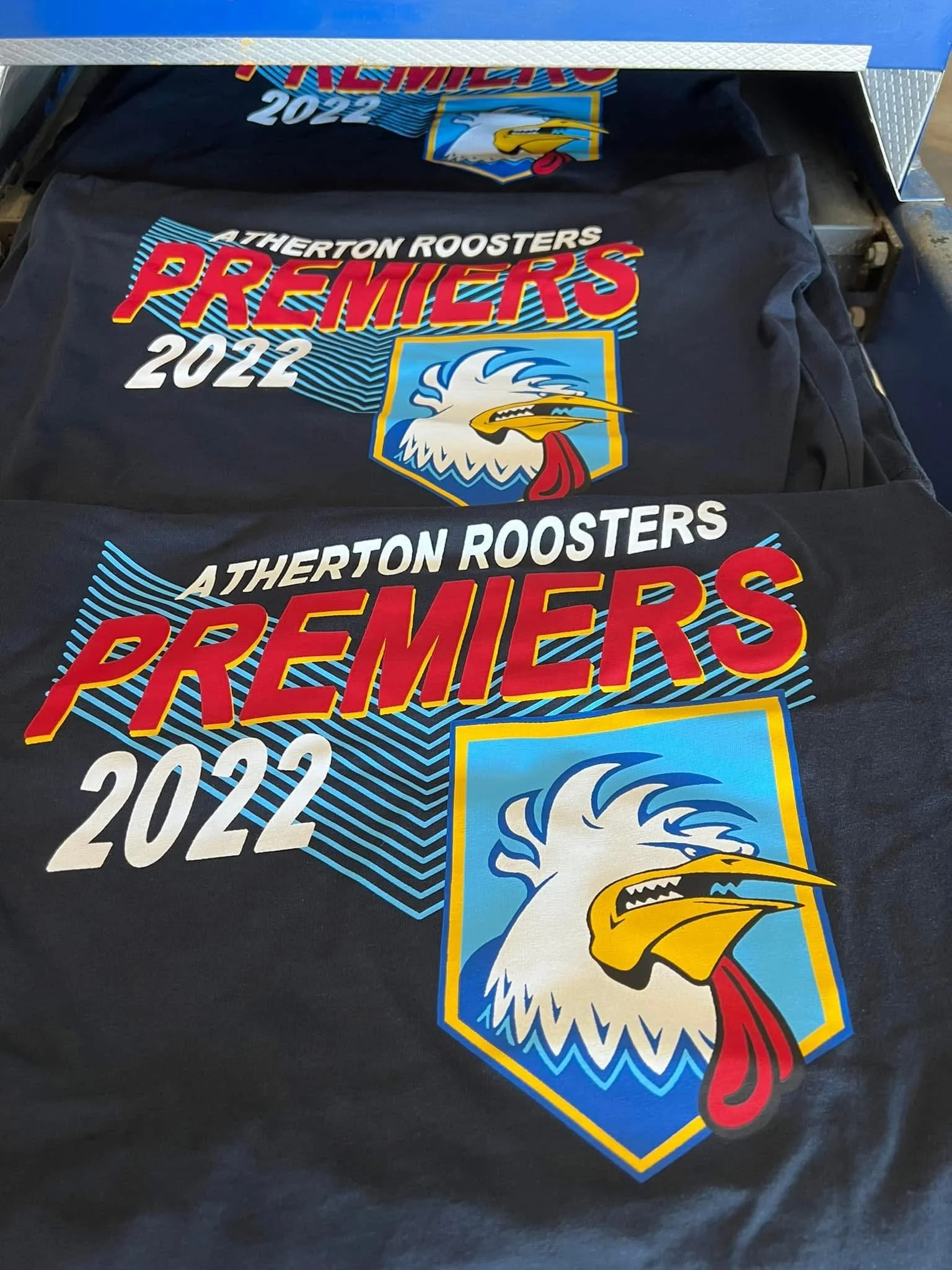 Black T-shirts with colorful design featuring a rooster, the text "Atherton Roosters Premiers 2022," and a sport emblem.