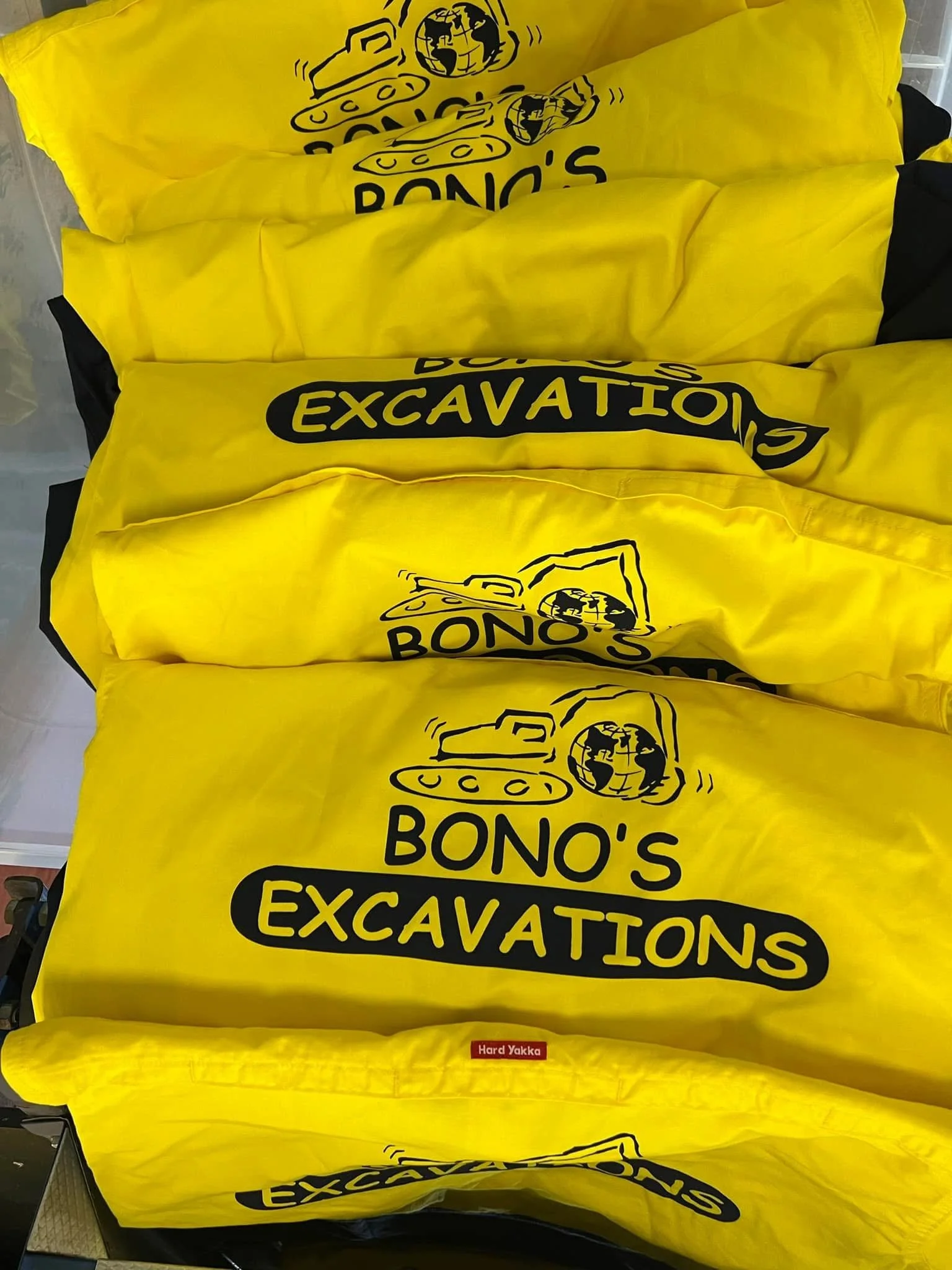 Yellow fabric covers with black printed logos for Bono's Excavations, featuring a tank graphic and a globe with shake hands