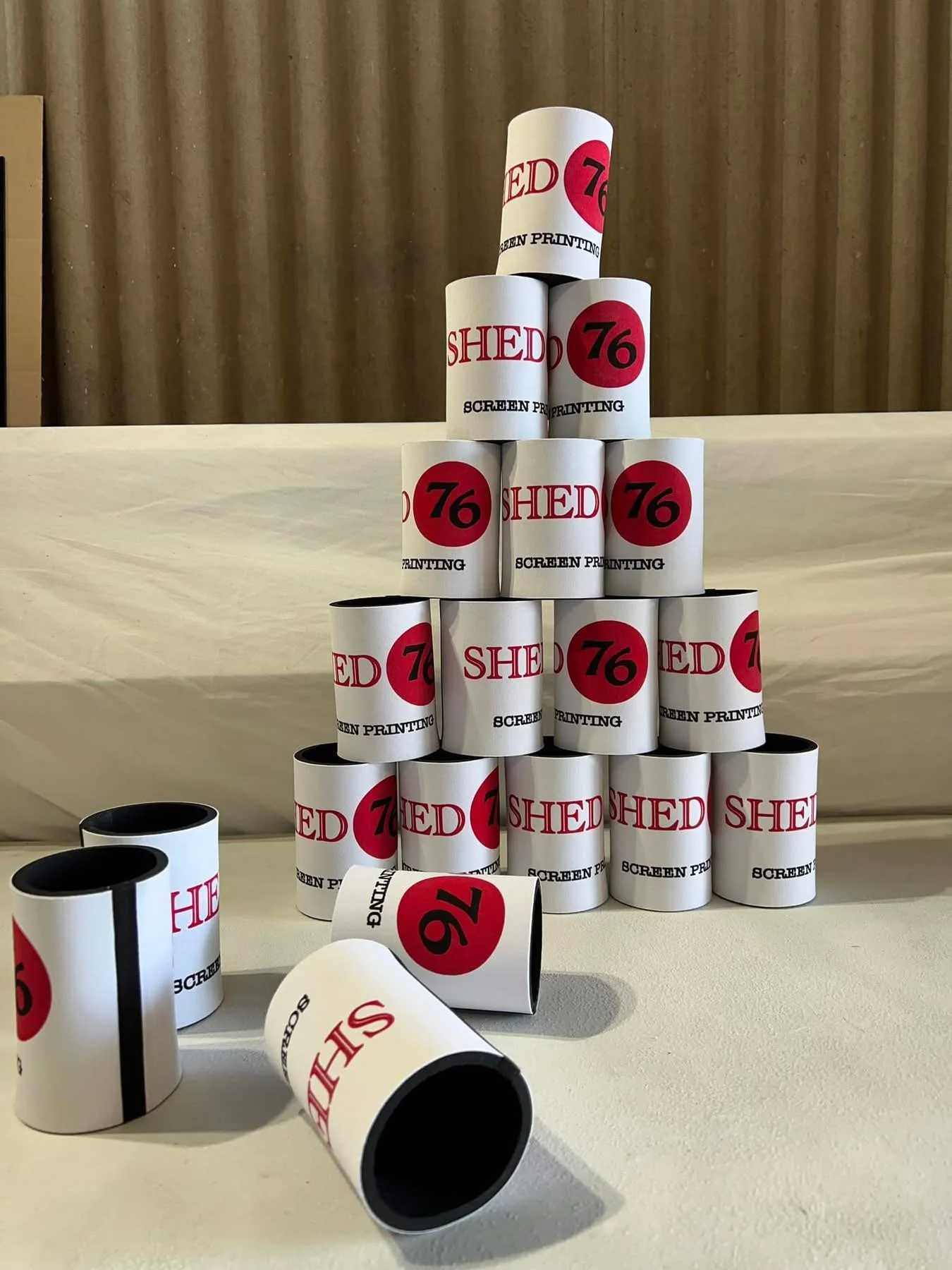 Stacked rolls of paper with printed text, forming a pyramid. The rolls feature the words "SHED 76 SCREEN PRINTING," with some rolls lying on the surface in front.