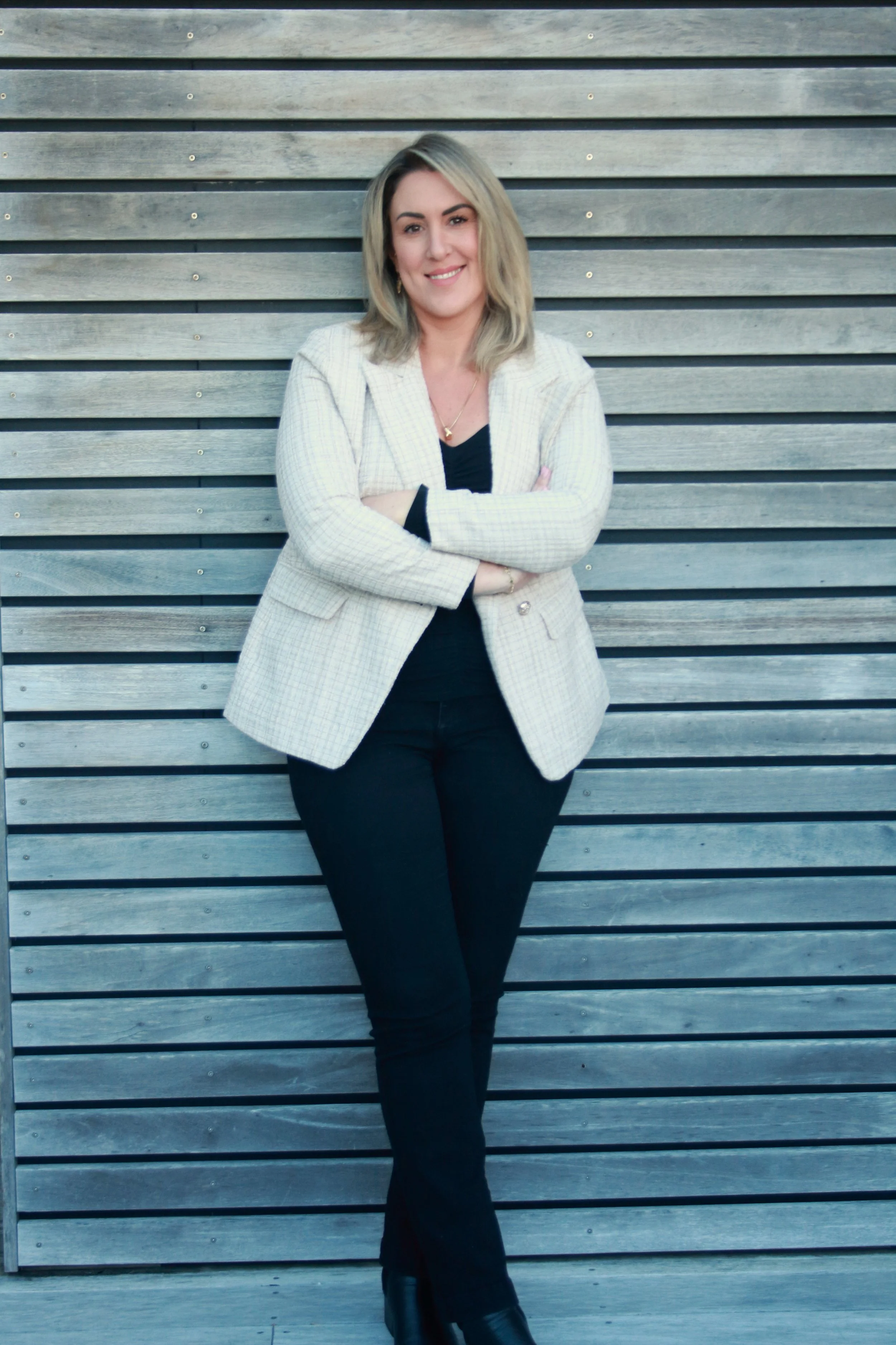 Genevieve Clasby, RTT Hypnotherapist and professional coach standing against a timber wall smiling with her arms crossed