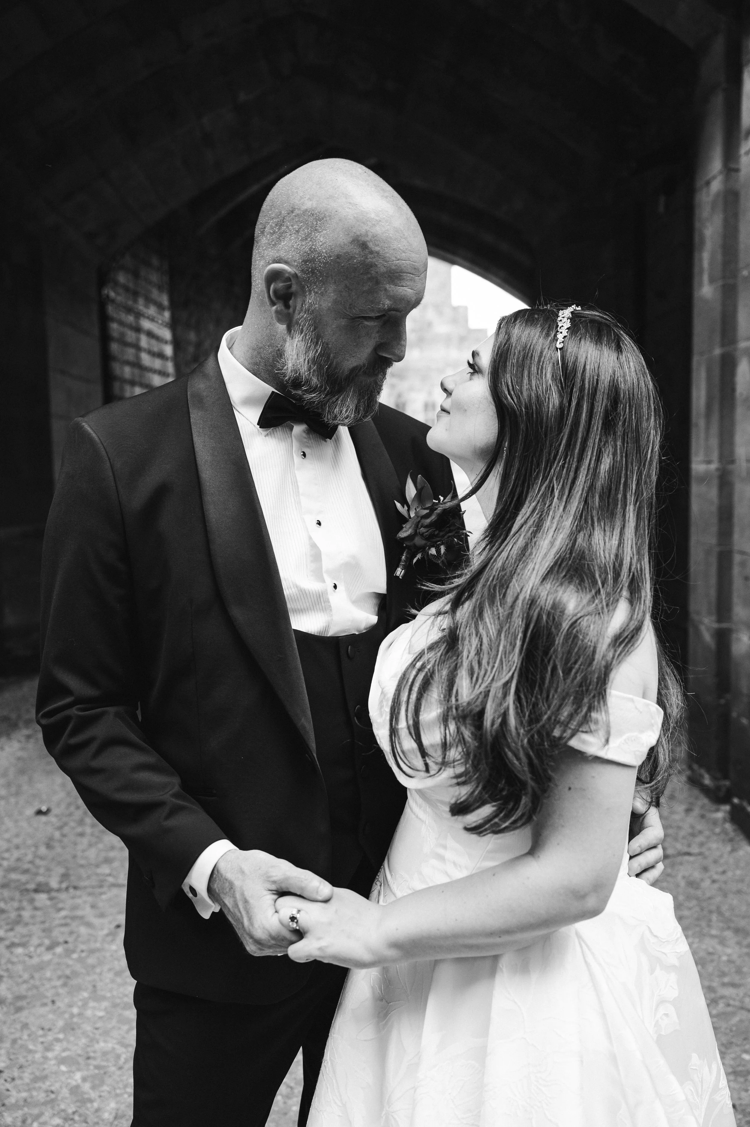 Peckforton Castle - black and white image of bride and groom in wedding holding each others hands in an archway