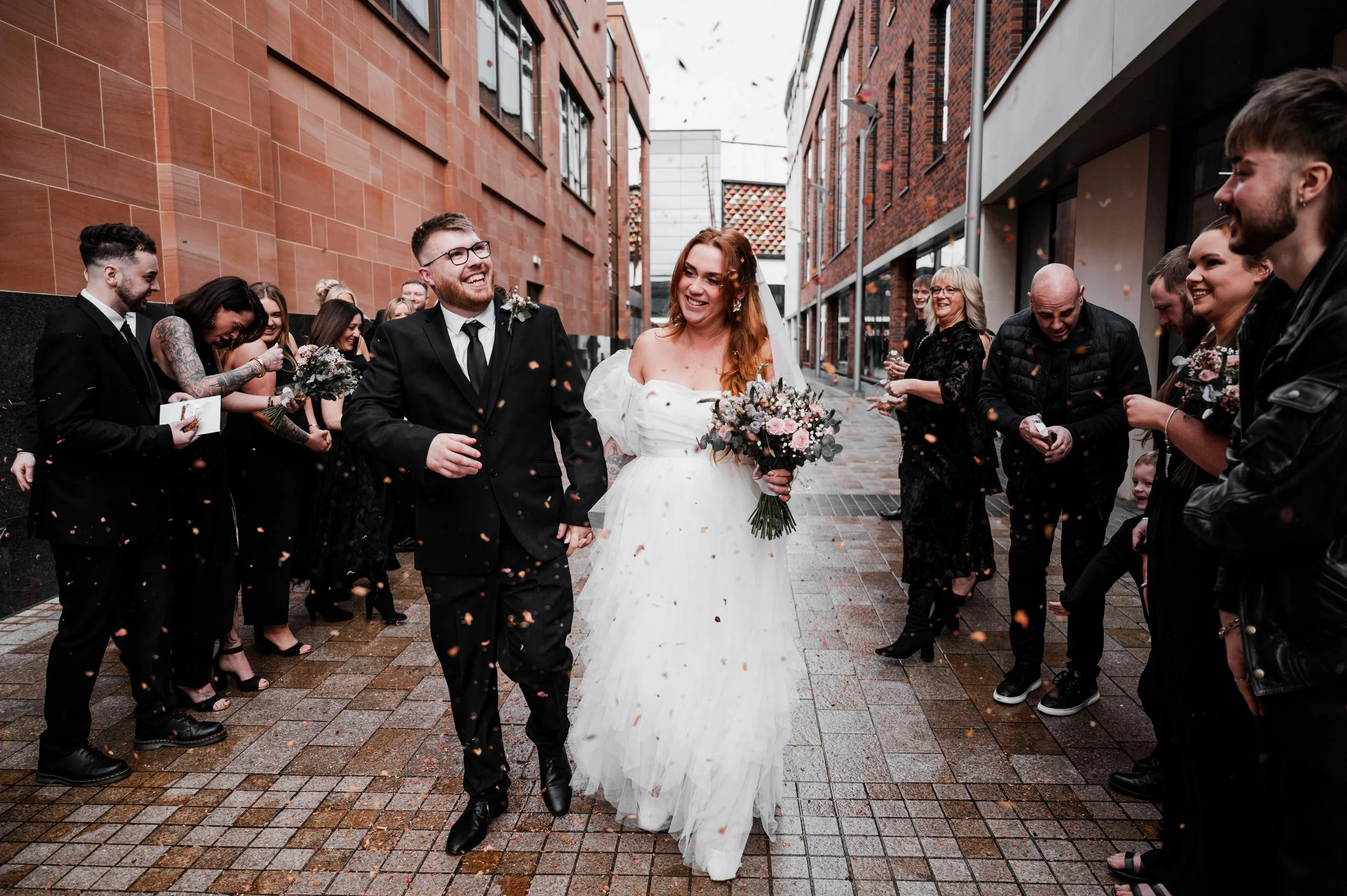 Wedding Photographer Cheshire - Bride and Groom in wedding attire walking down street surrounded by wedding guests throwing confetti