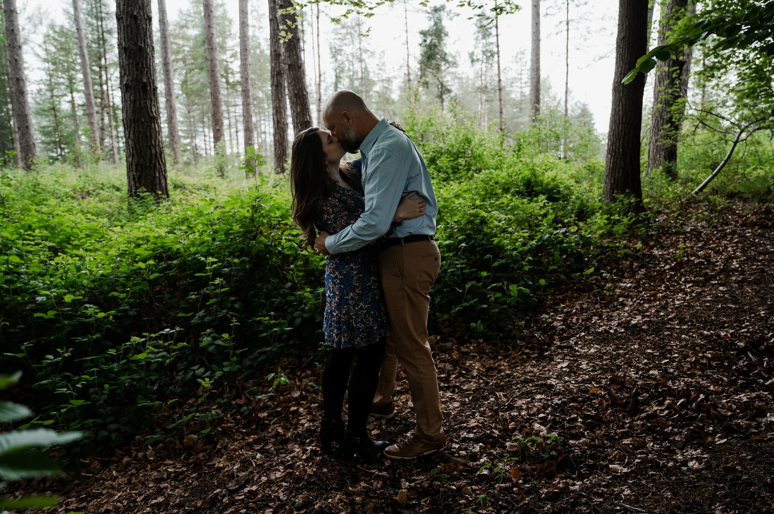 Delamere Forest Engagement shoot - man and woman embraced and kissing with woodland behind them
